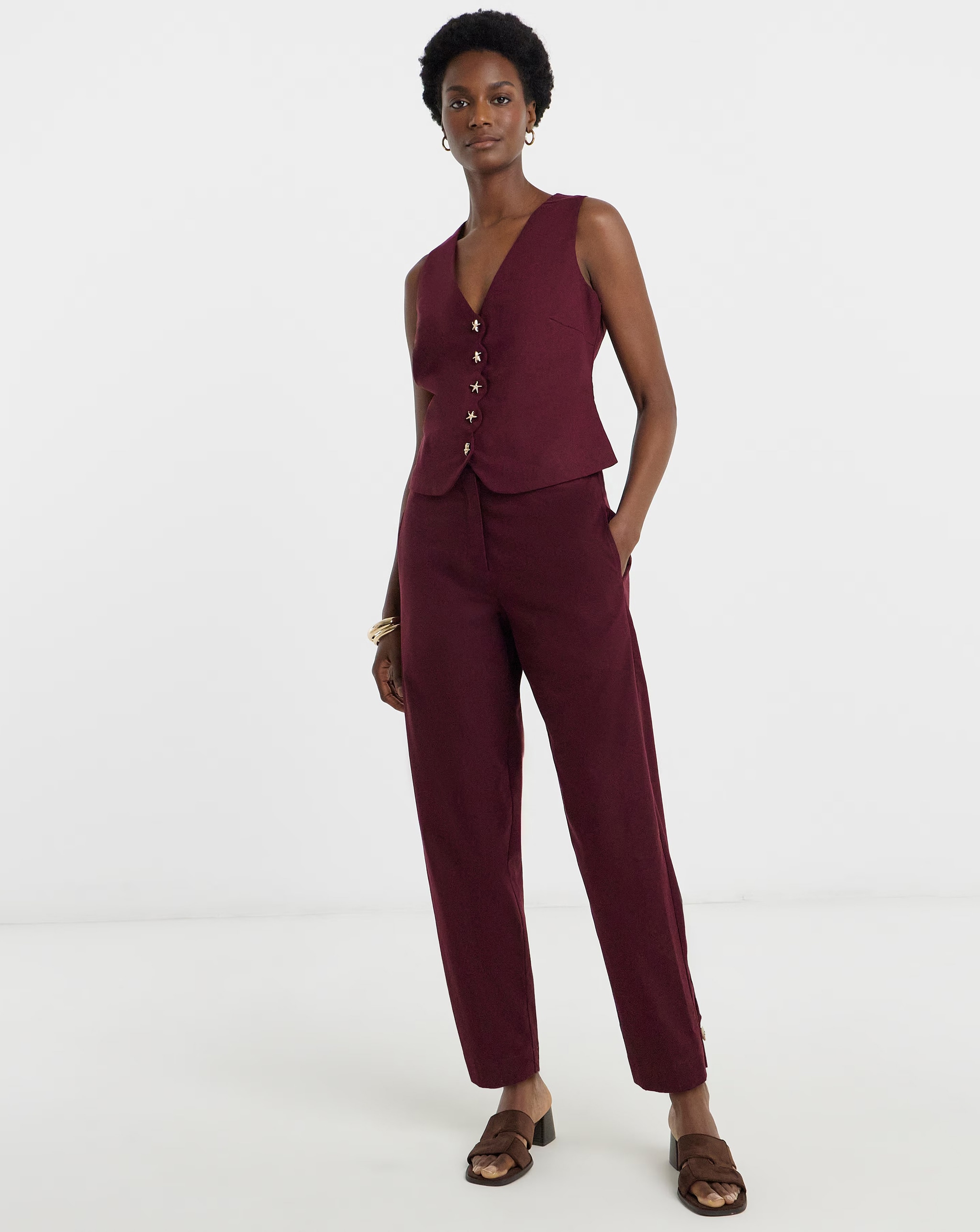 Person standing in a burgundy buttoned vest with matching tailored trousers.