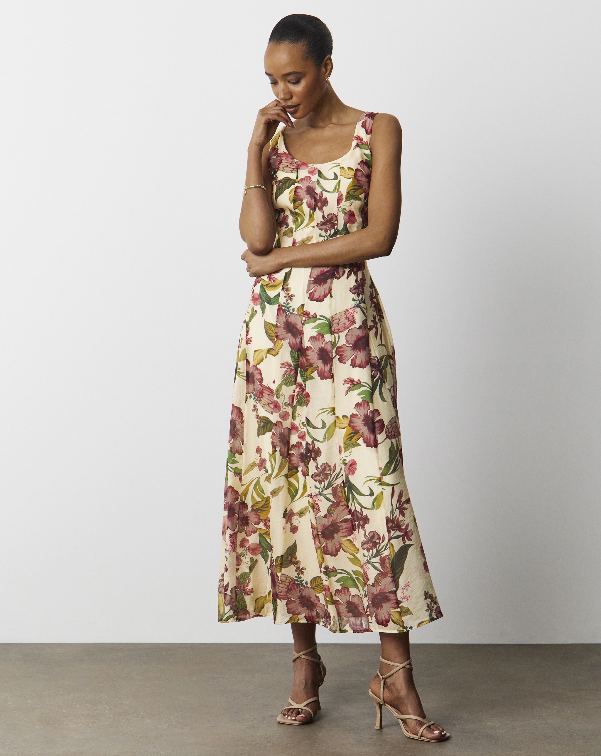 A lady wearing a cream dress with colourful floral patterns on.