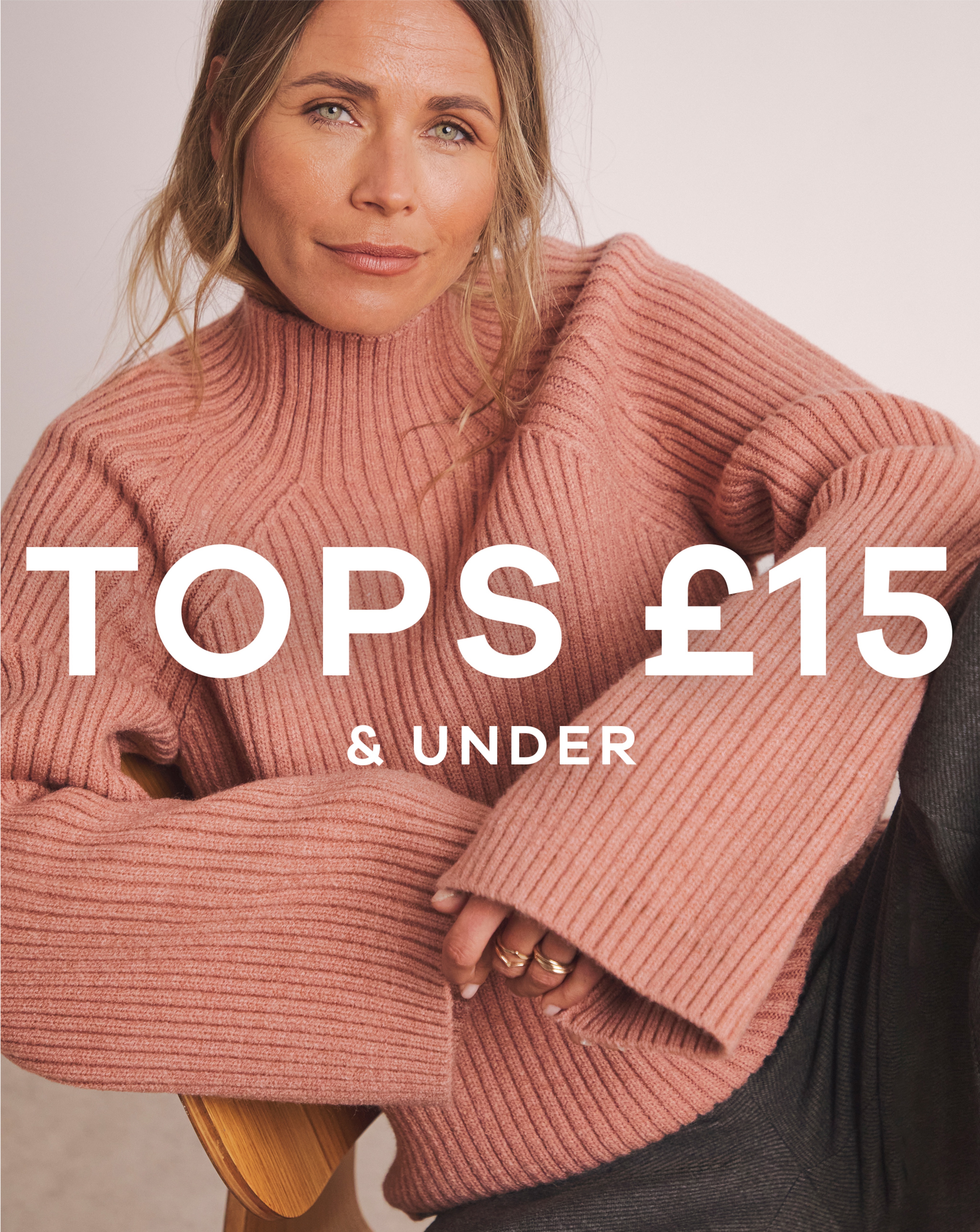 A woman sat leaning on a chair wearing a blush pink knitted jumper.