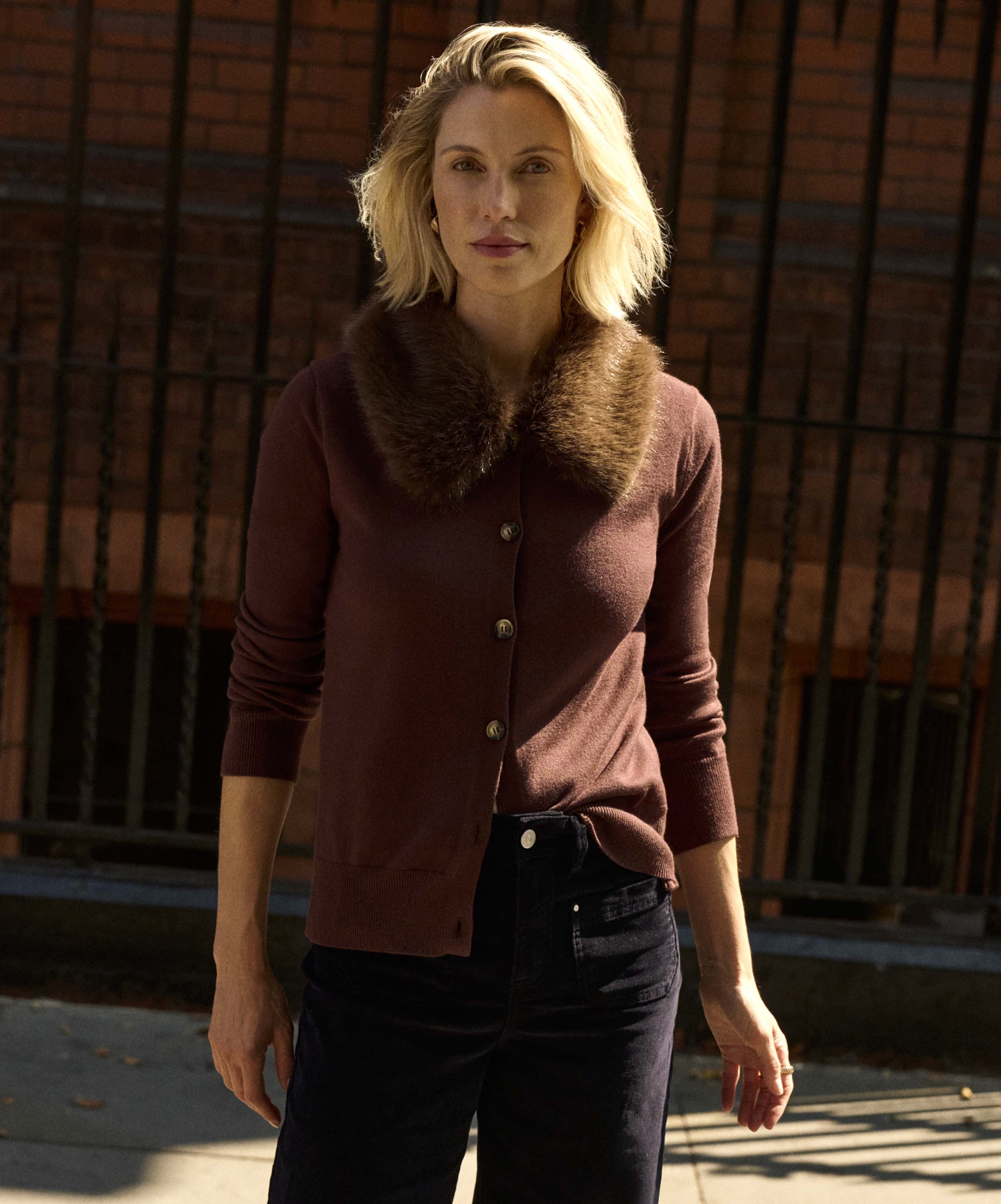 A woman stood outside wearing a brown cardigan with a faux fur collar.