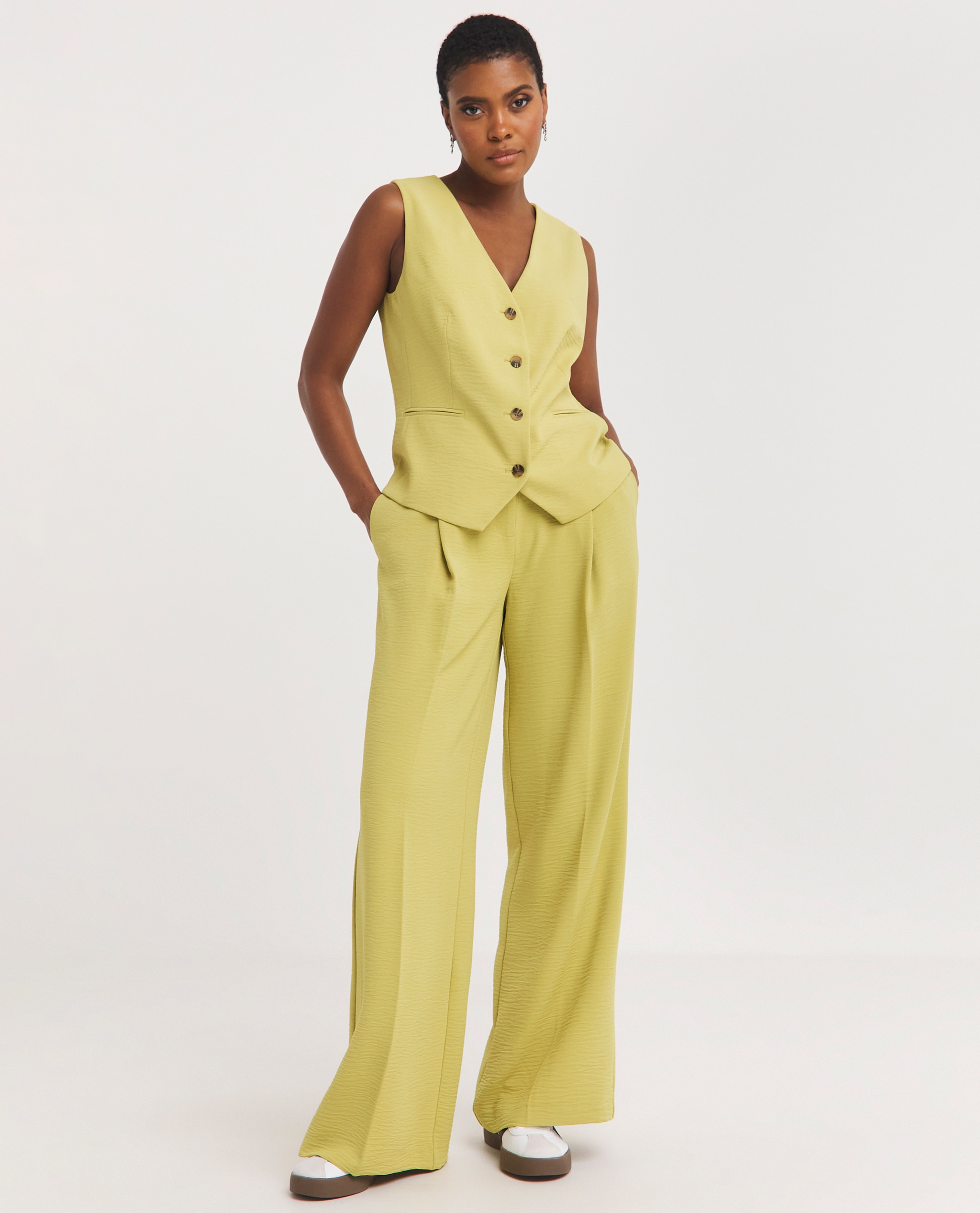 Model is wearing a yellow linen button through waistcoat with matching yellow linen trousers.