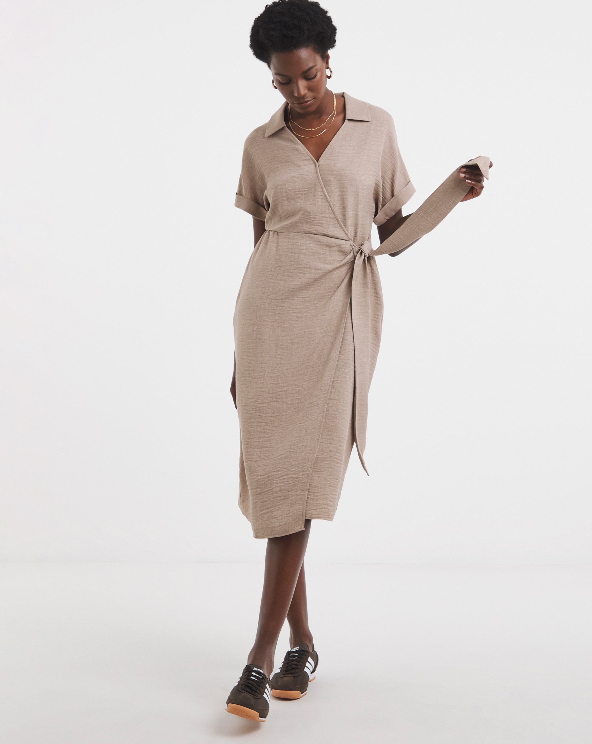 Person wearing a beige short‑sleeve wrap‑style midi dress with a waist tie.