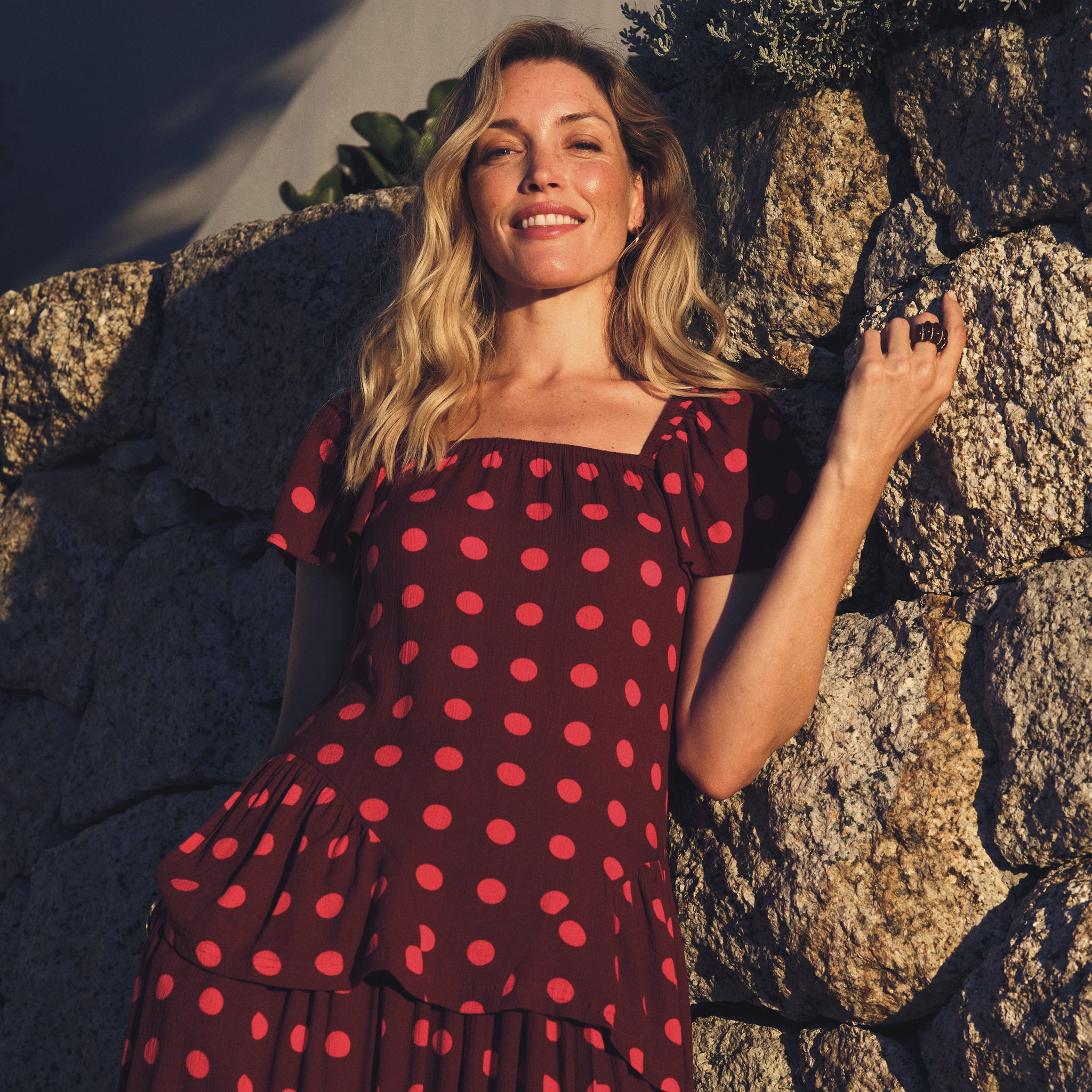 A lady wearing a dark red dress with bright red spots on it.
