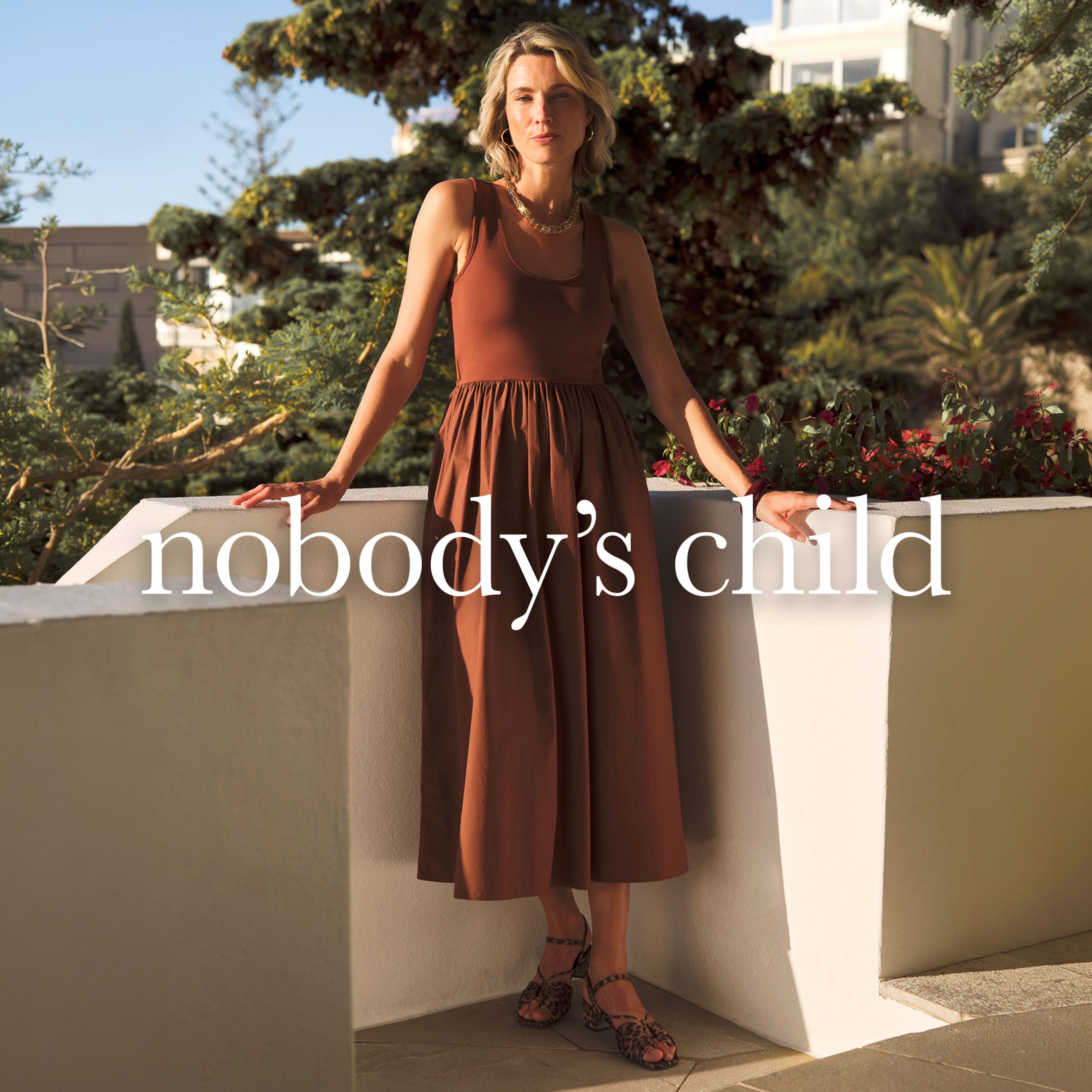 A lady wearing brown dress leaning against a wall