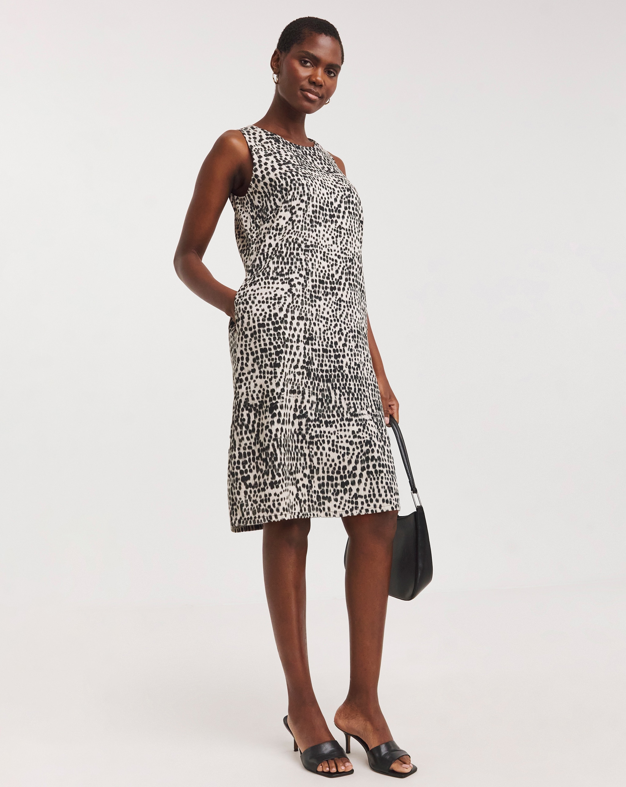 Person wearing a sleeveless black and white patterned knee‑length dress with black shoes.