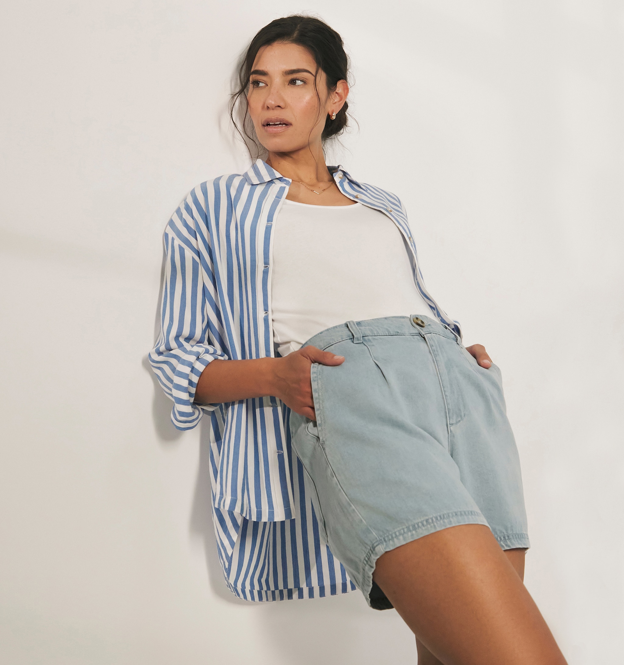 Woman stood wearing a striped blue and white shirt over a white t shirt with light blue shorts