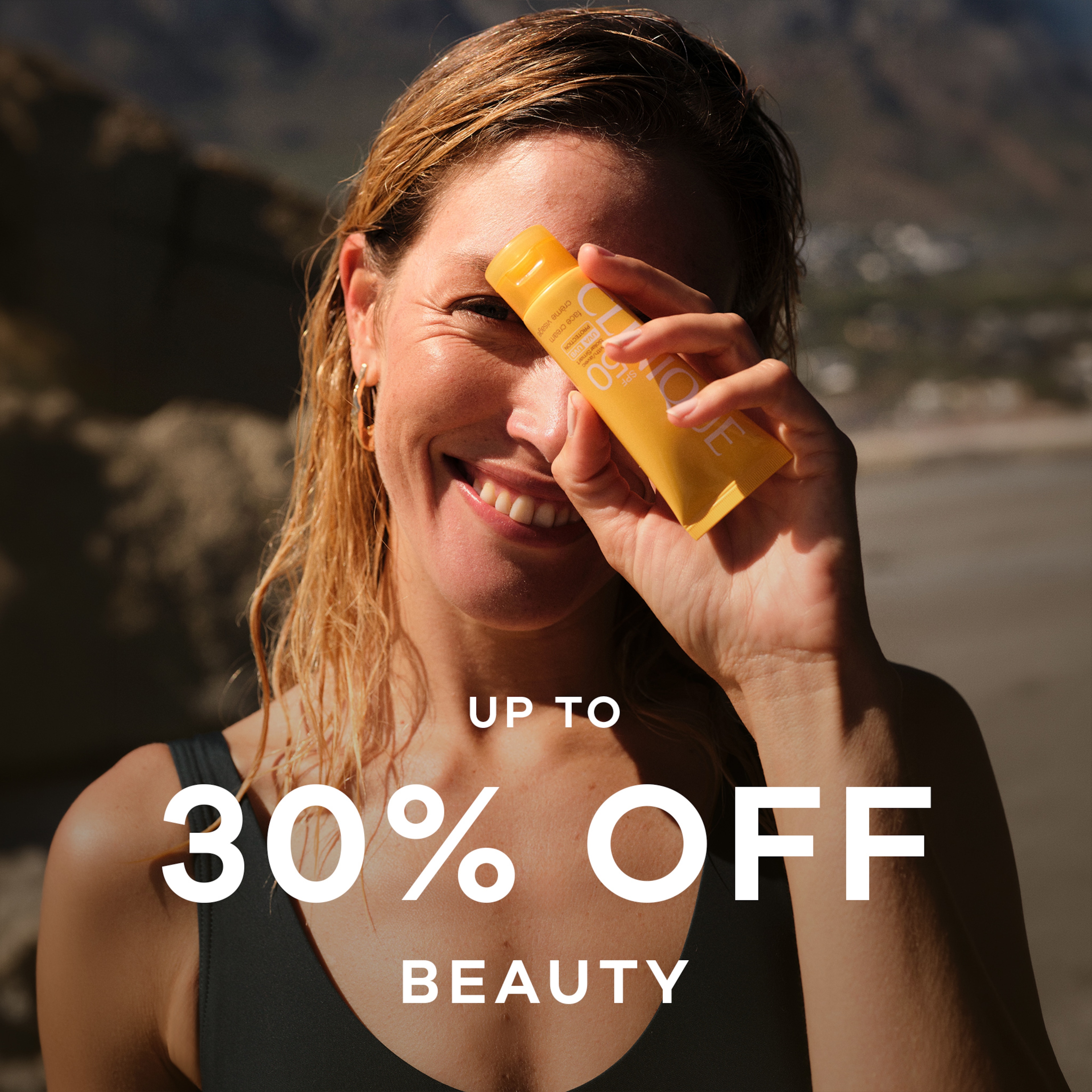 A lady wearing a black swimsuit holding a beauty product in front of her face.