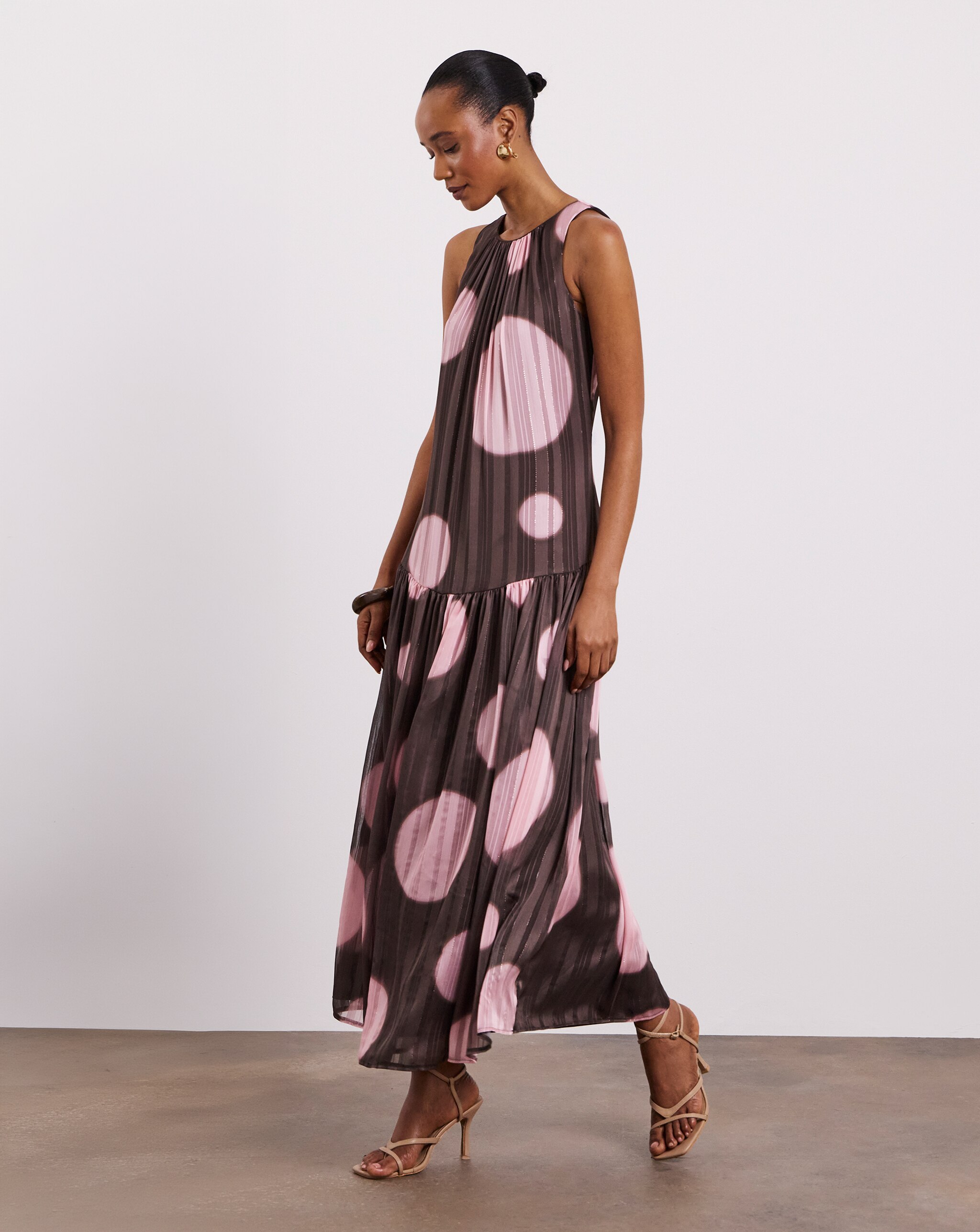 Person wearing a sleeveless Joanna Hope midi dress with a brown and pink oversized polka-dot print, nude strappy heels, and gold earrings.