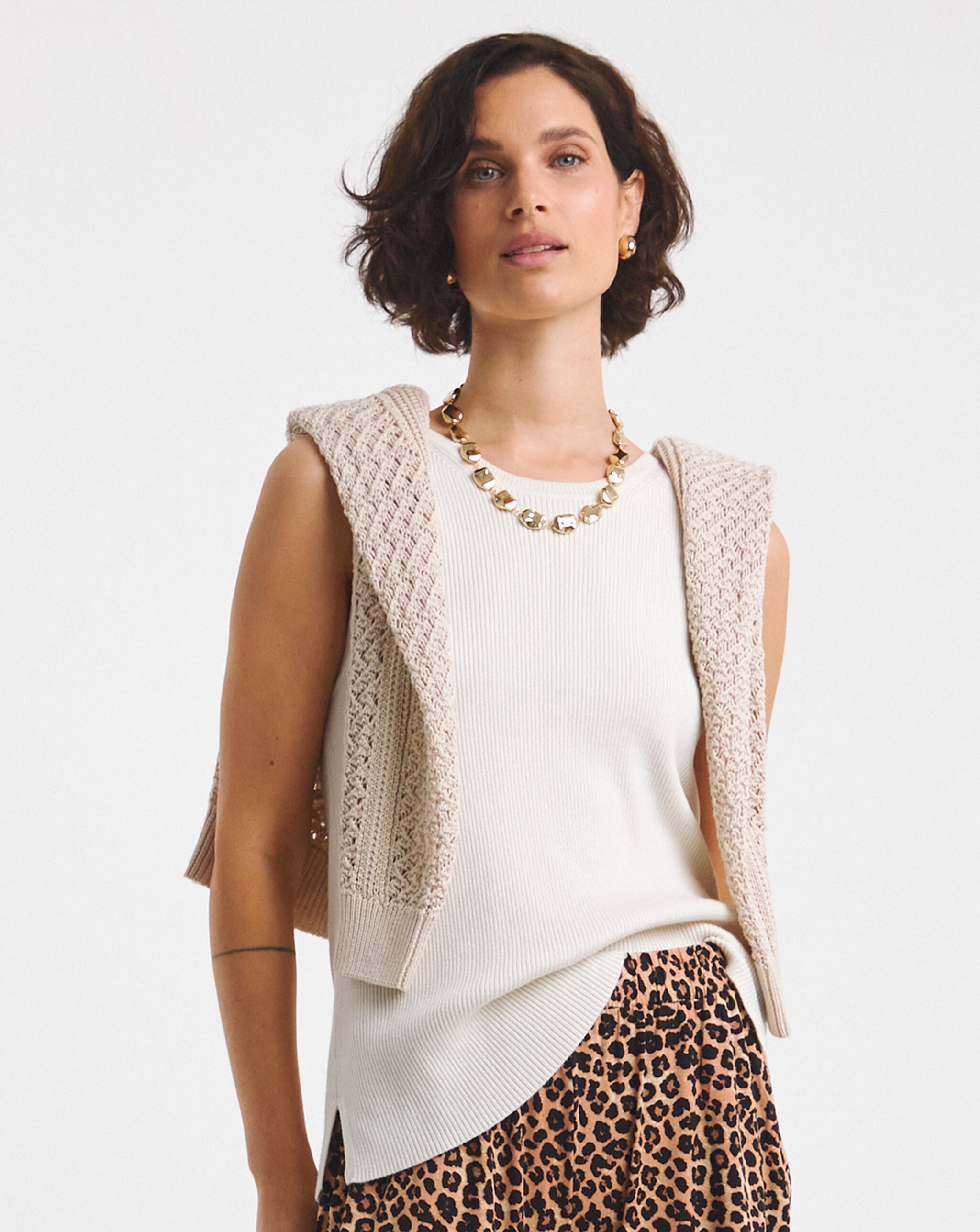 Person wearing a white sleeveless top, knit vest, and leopard‑print wide‑leg trousers.