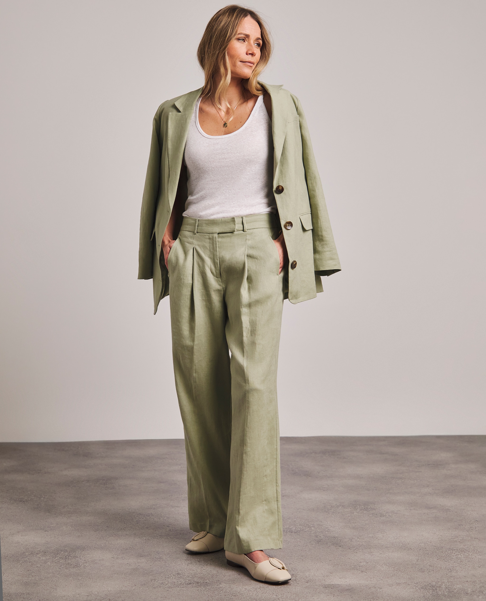 Model is wearing a green linen blazer with a white t-shirt underneath with a pair of green linen trousers.