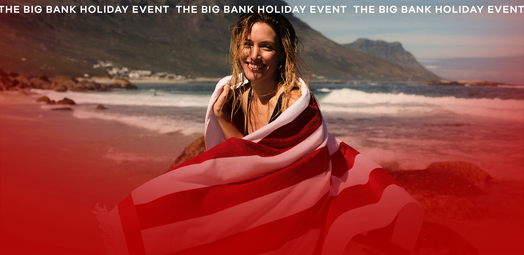 A lady smiling wrapped in a a red and white striped towel on a beach