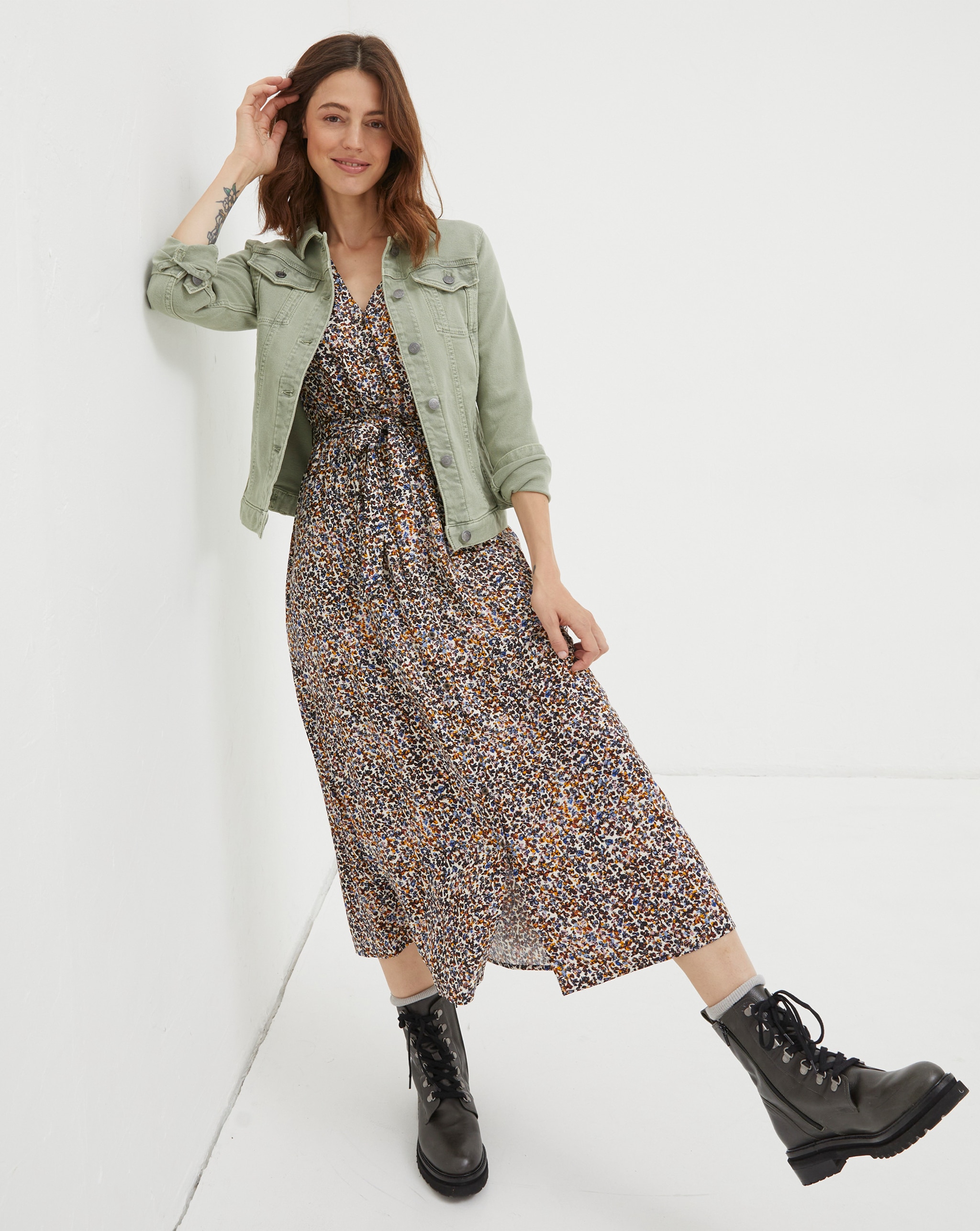 Person wearing a sage green denim jacket over a printed maxi dress, styled with black lace-up ankle boots.