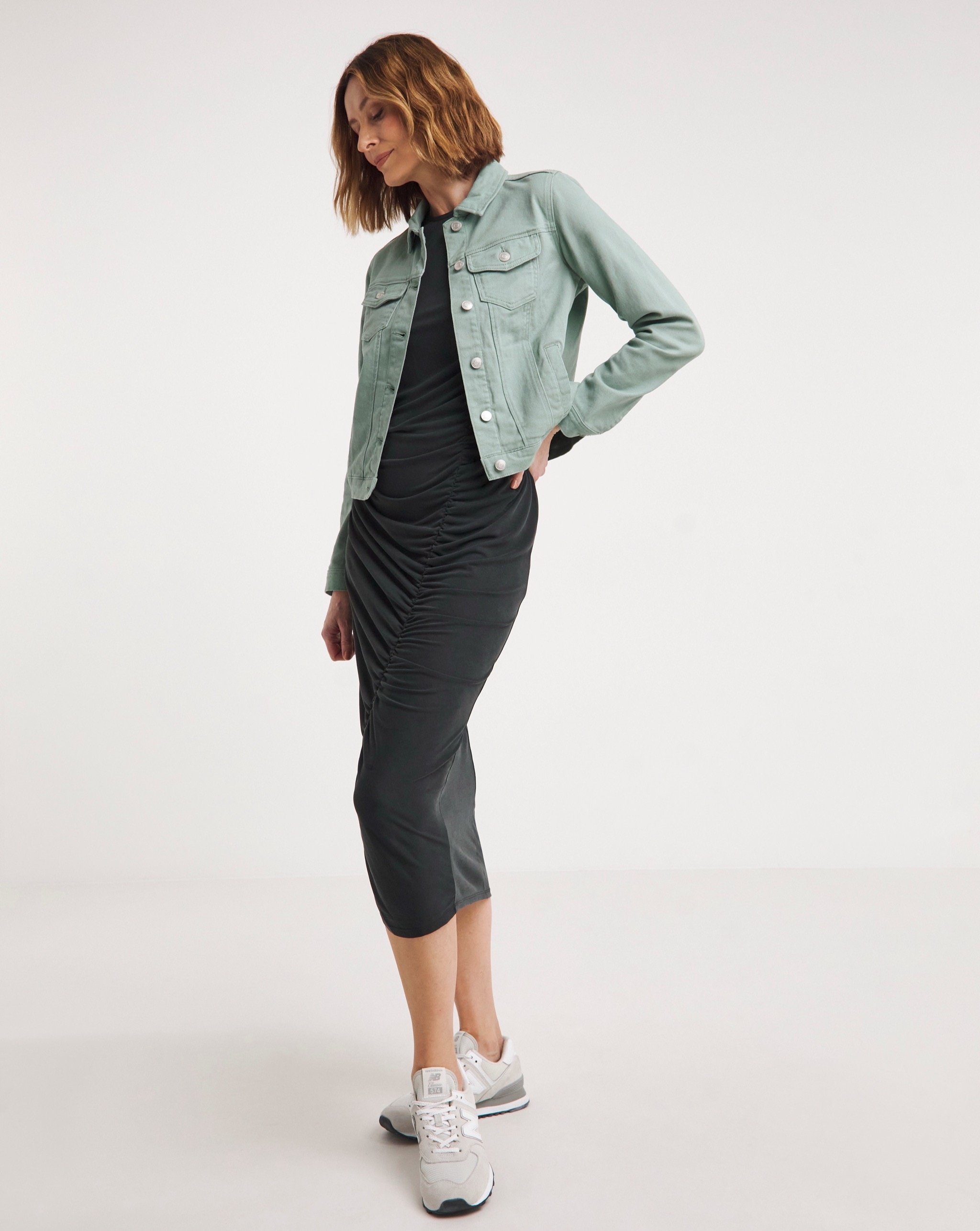 Person wearing a sage green denim jacket over a midi dress, paired with white trainers.