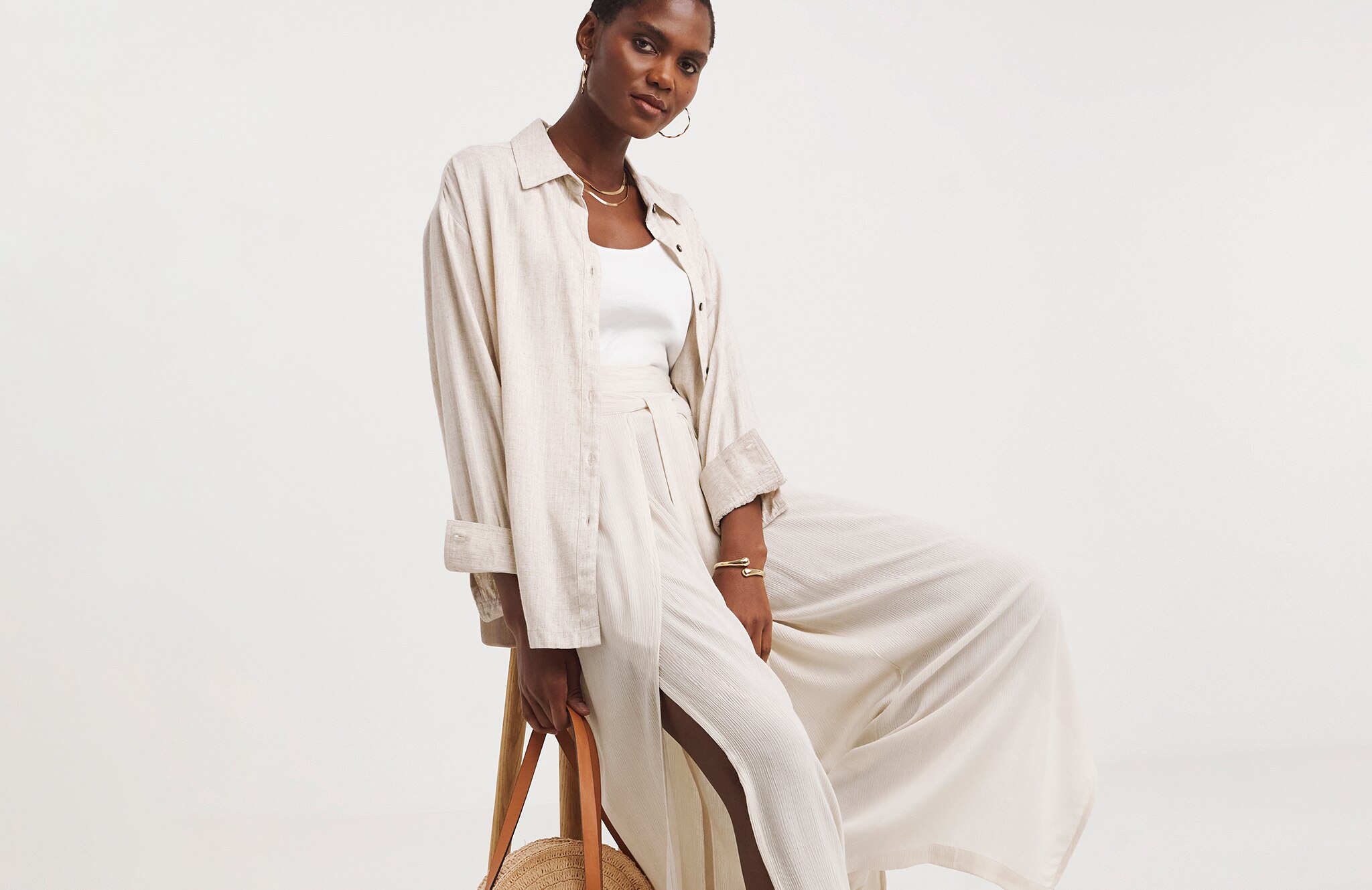 Model is wearing a cream linen shirt over a white t-shirt with a pair of cream trousers.