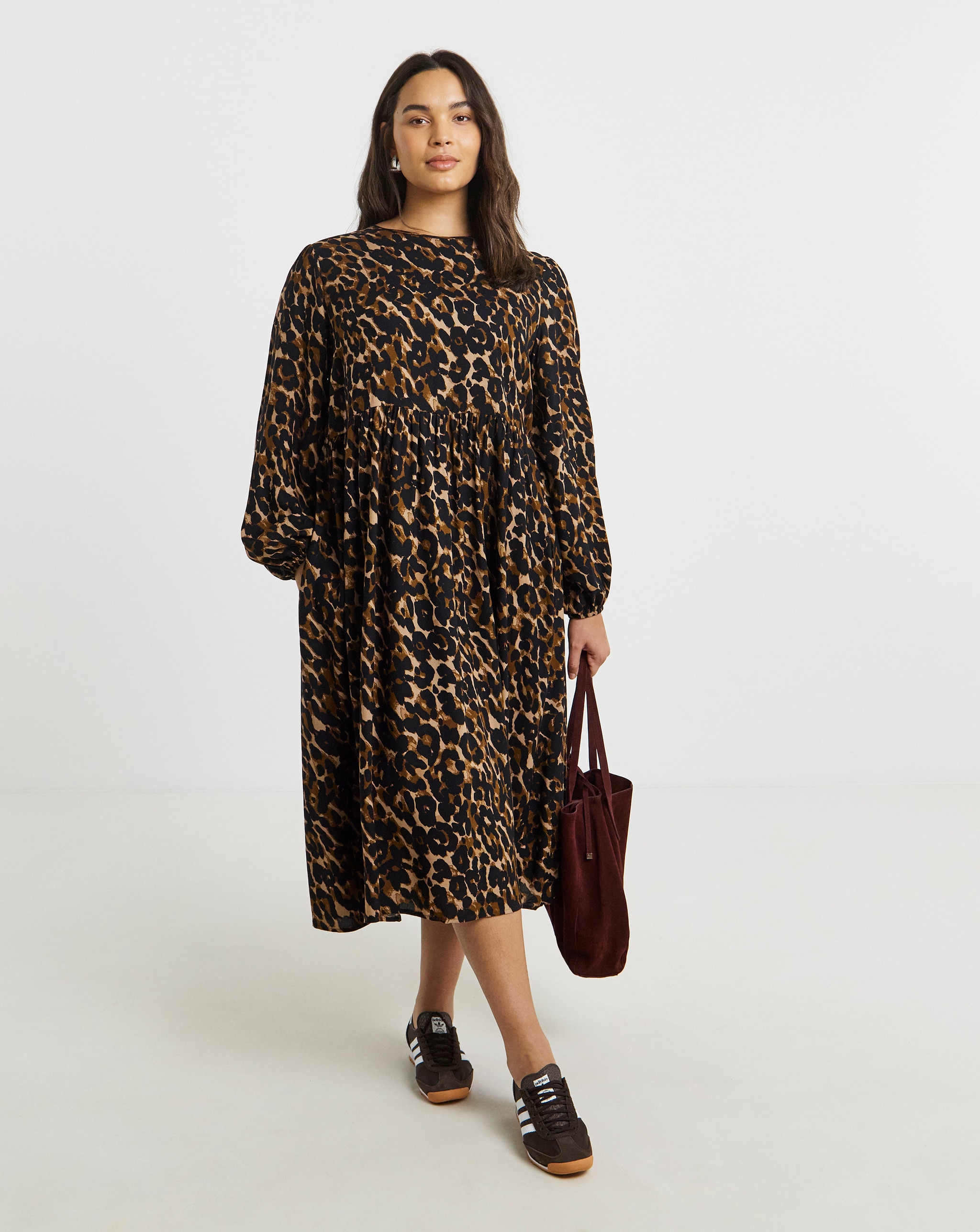 Person wearing a black and brown leopard-print midi dress with long sleeves, carrying a burgundy tote bag.