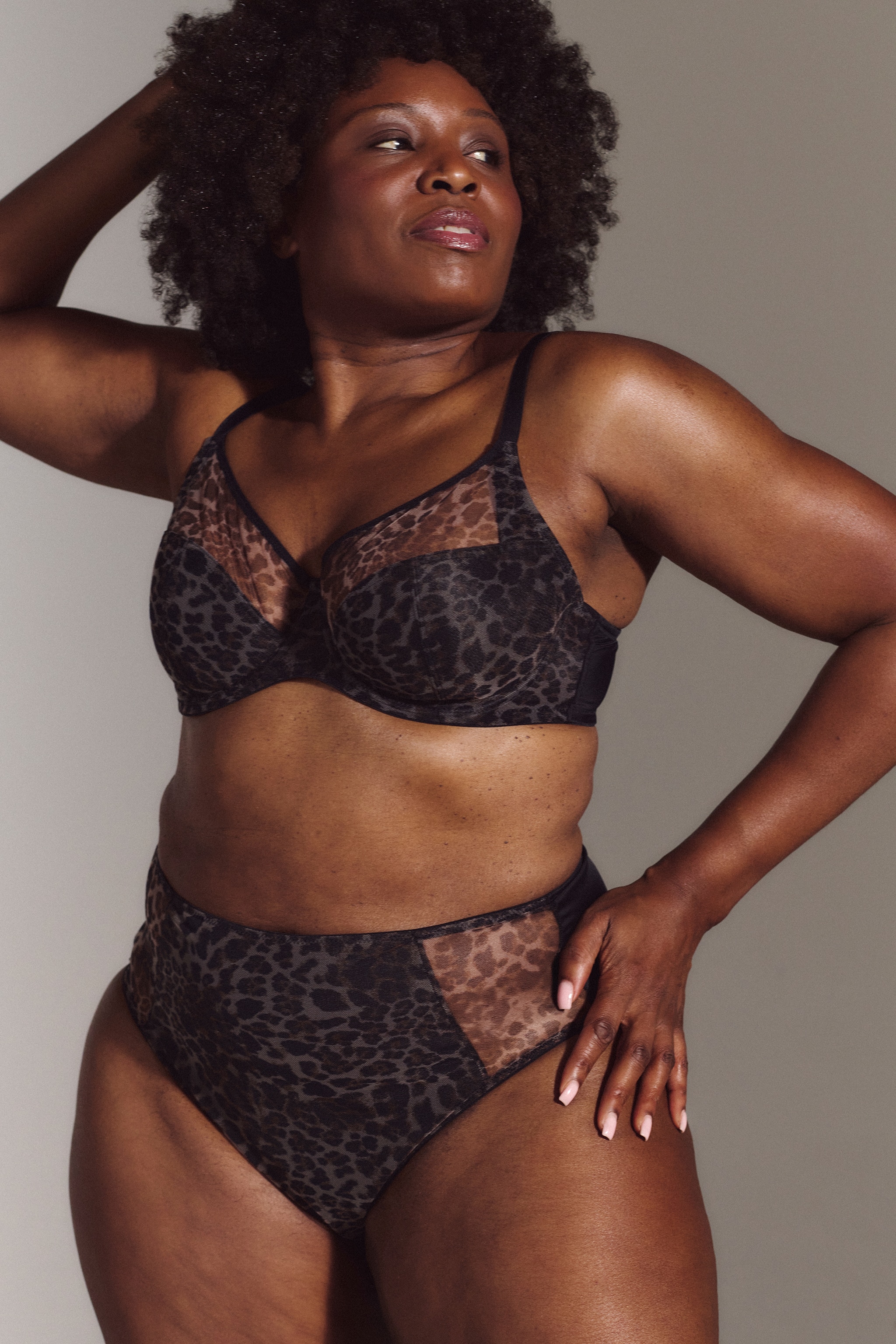 A woman stood with one hand on her hip and the other on her head wearing matching black lingerie.