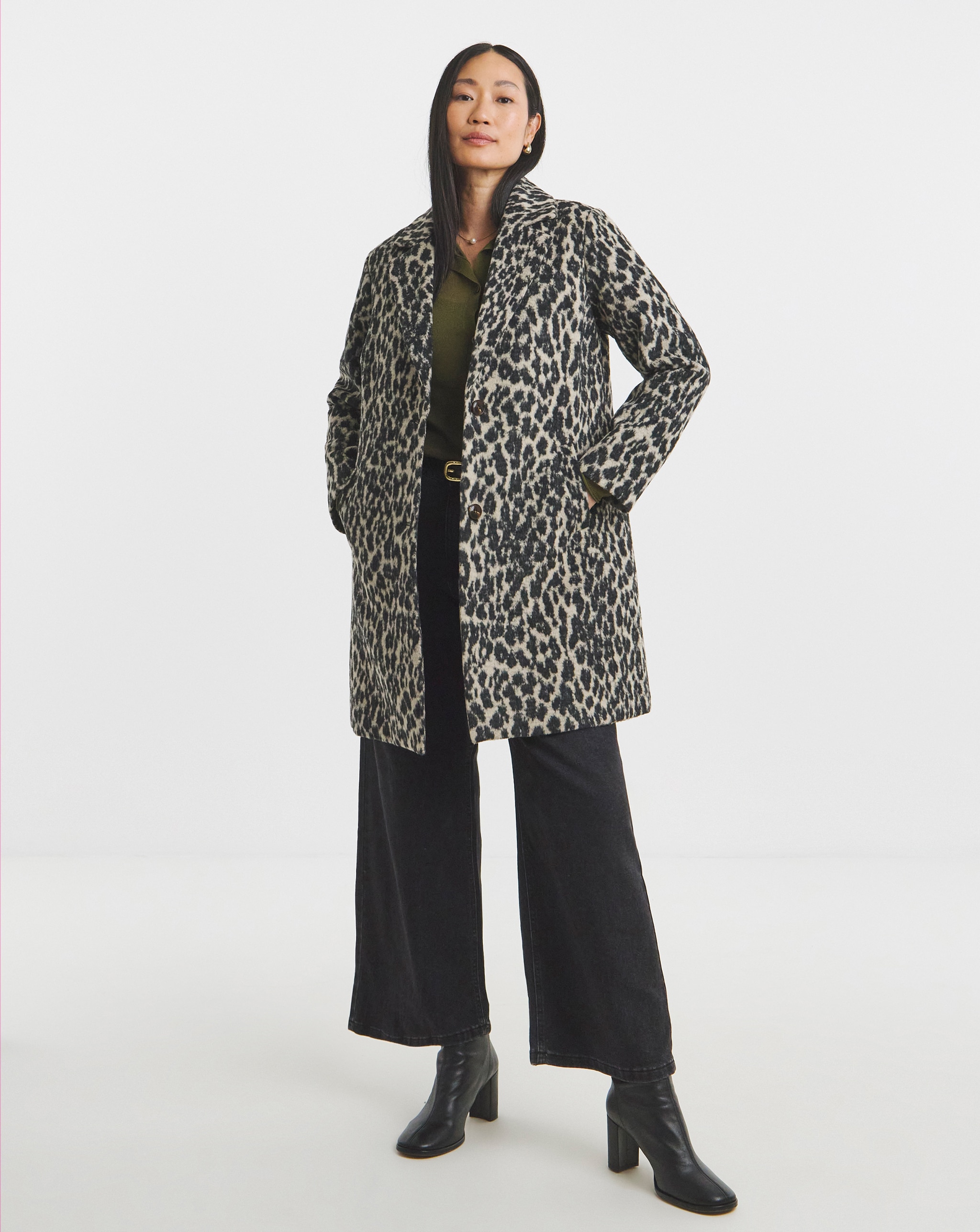 Person wearing a leopard‑print coat over a dark top, wide‑leg black trousers and black ankle boots, with hands in coat pockets. 