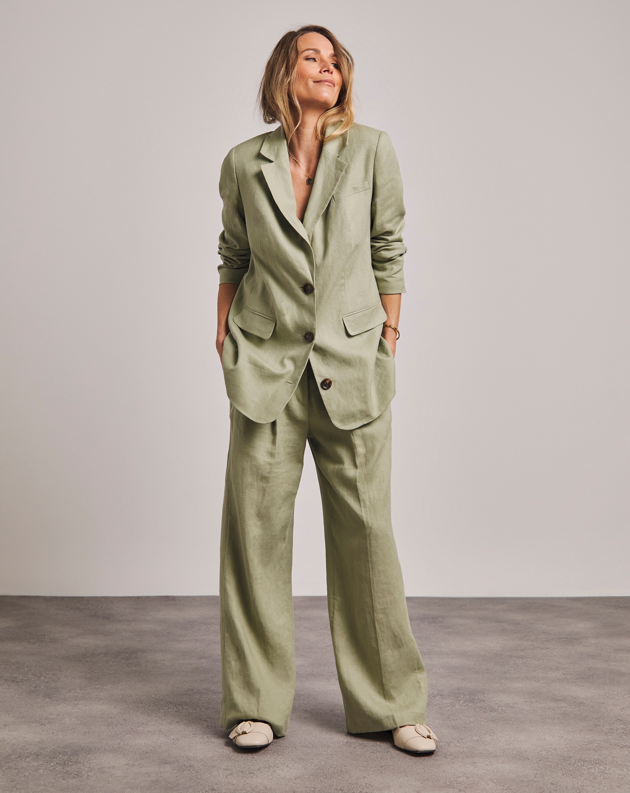 Person standing in a light green suit with a long blazer and wide‑leg trousers.