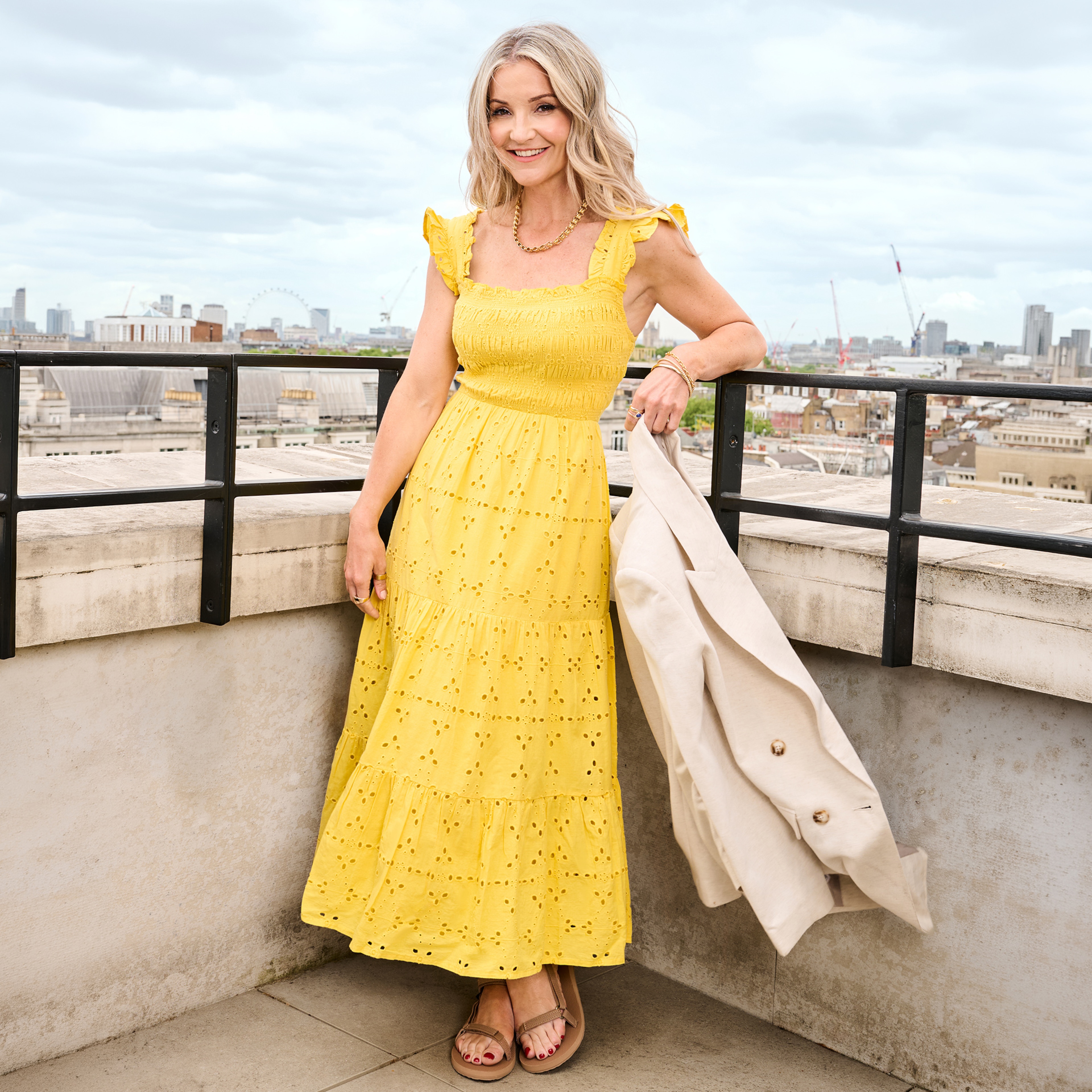 Helen Skelton wearing a yellow dress stood on a balcony.