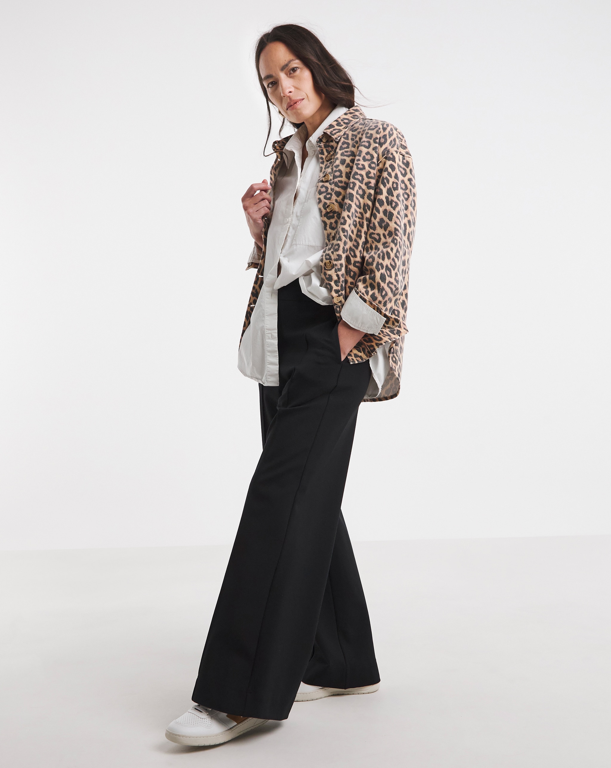 Person wearing a cropped leopard-print jacket layered over a white shirt with black wide-leg trousers and white trainers.