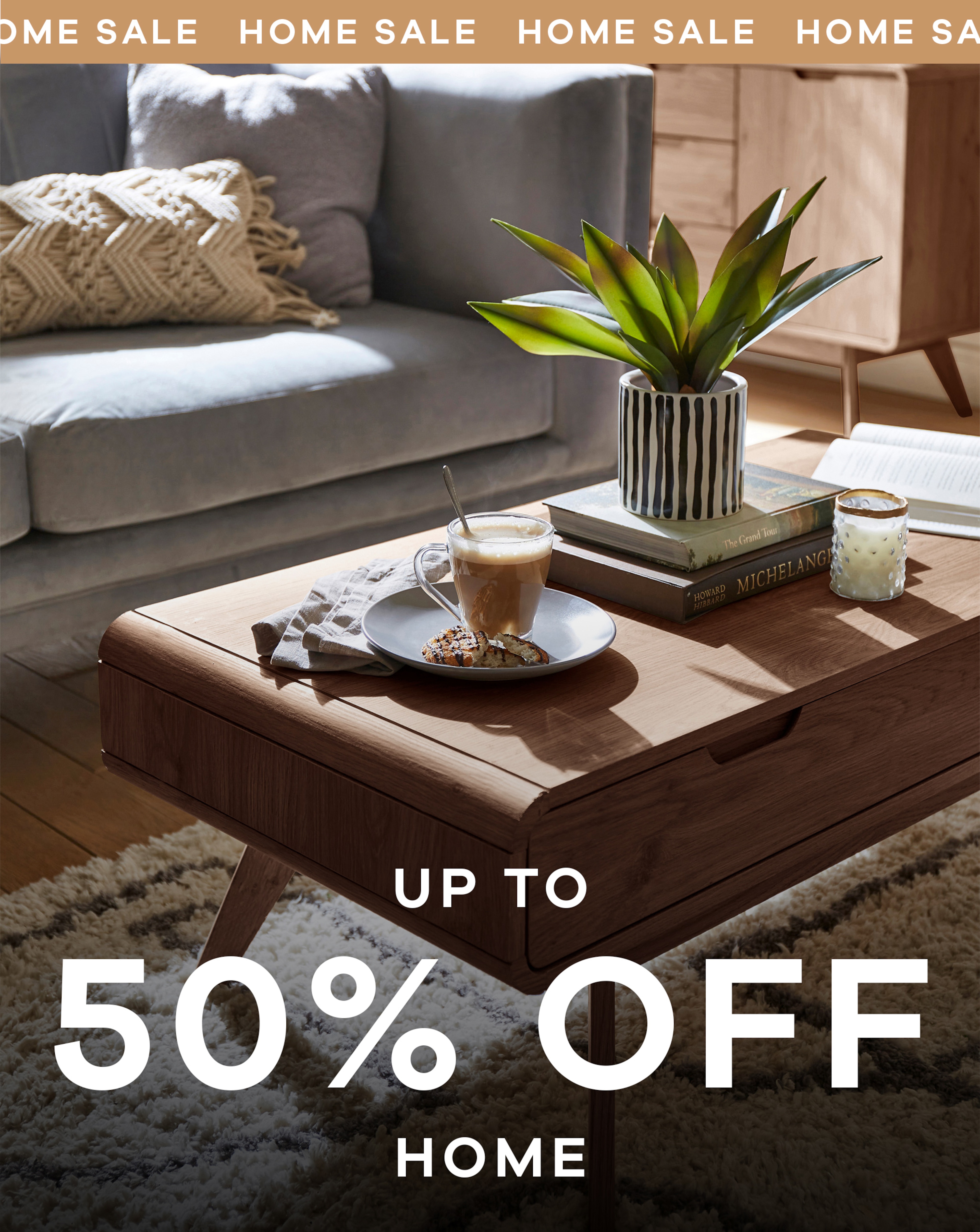A livingroom. A grey sofa in the background with a brown wood coffee table with a coffee, plant and a candle on it.
