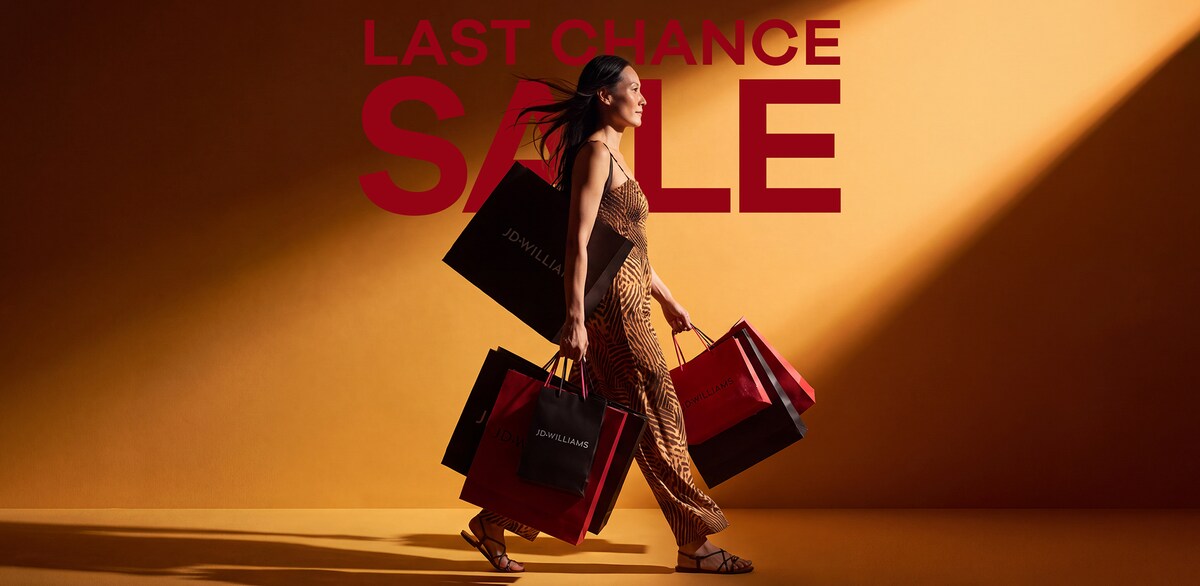 A woman walking with lots of JD Williams shopping bags in front of a orangey yellow background with the word 'SALE' on it in white