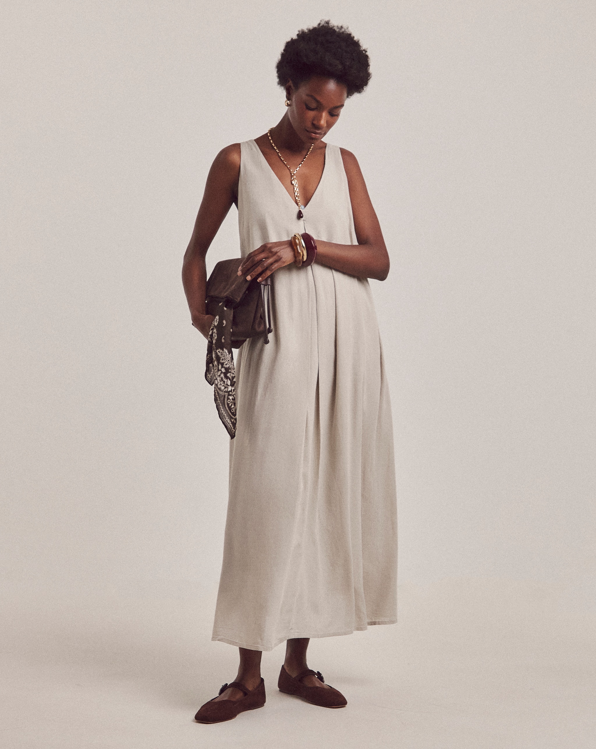 A woman wearing a stone coloured sleeveless dress holding a hand bag
