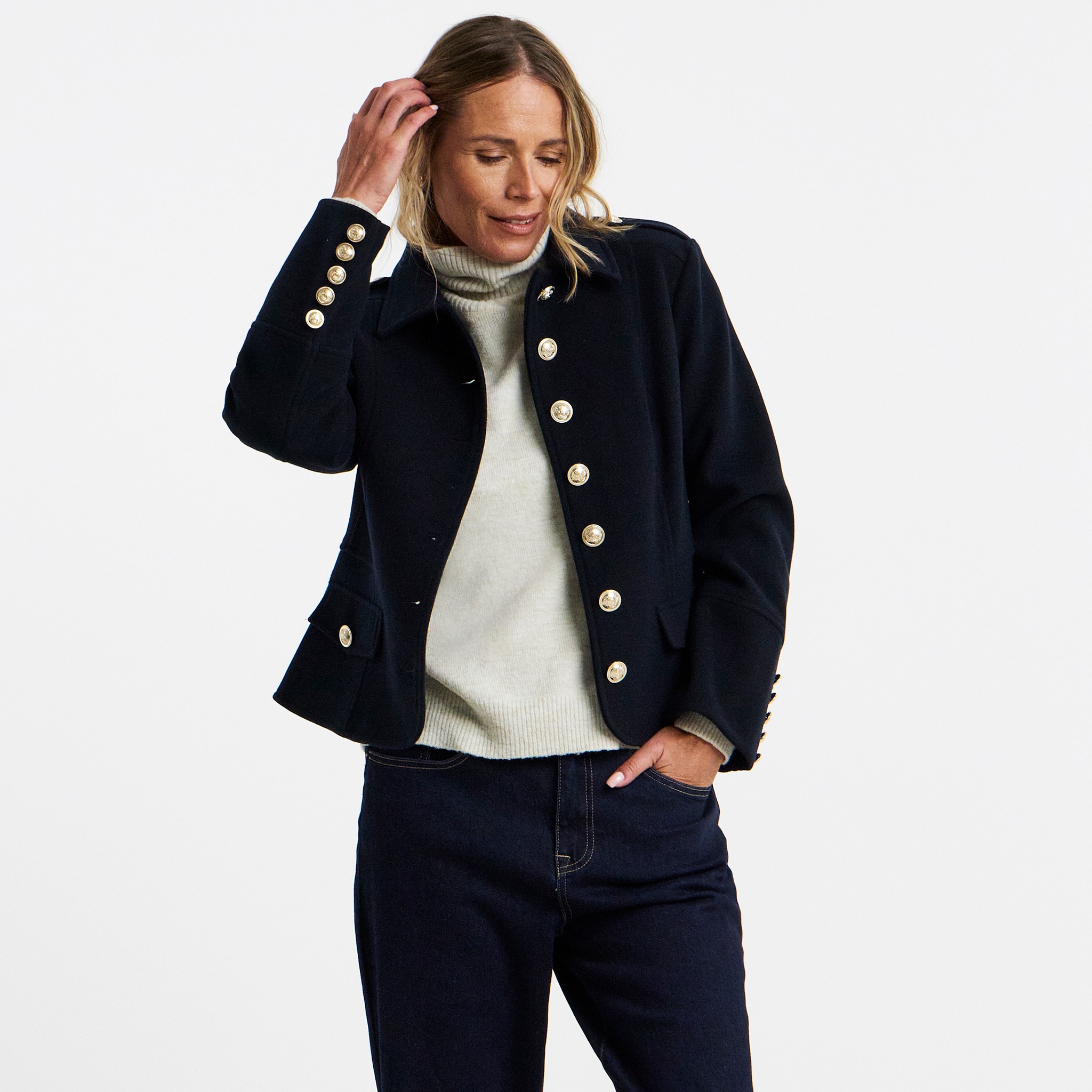 A woman stood wearing a short jacket with big brass buttons.