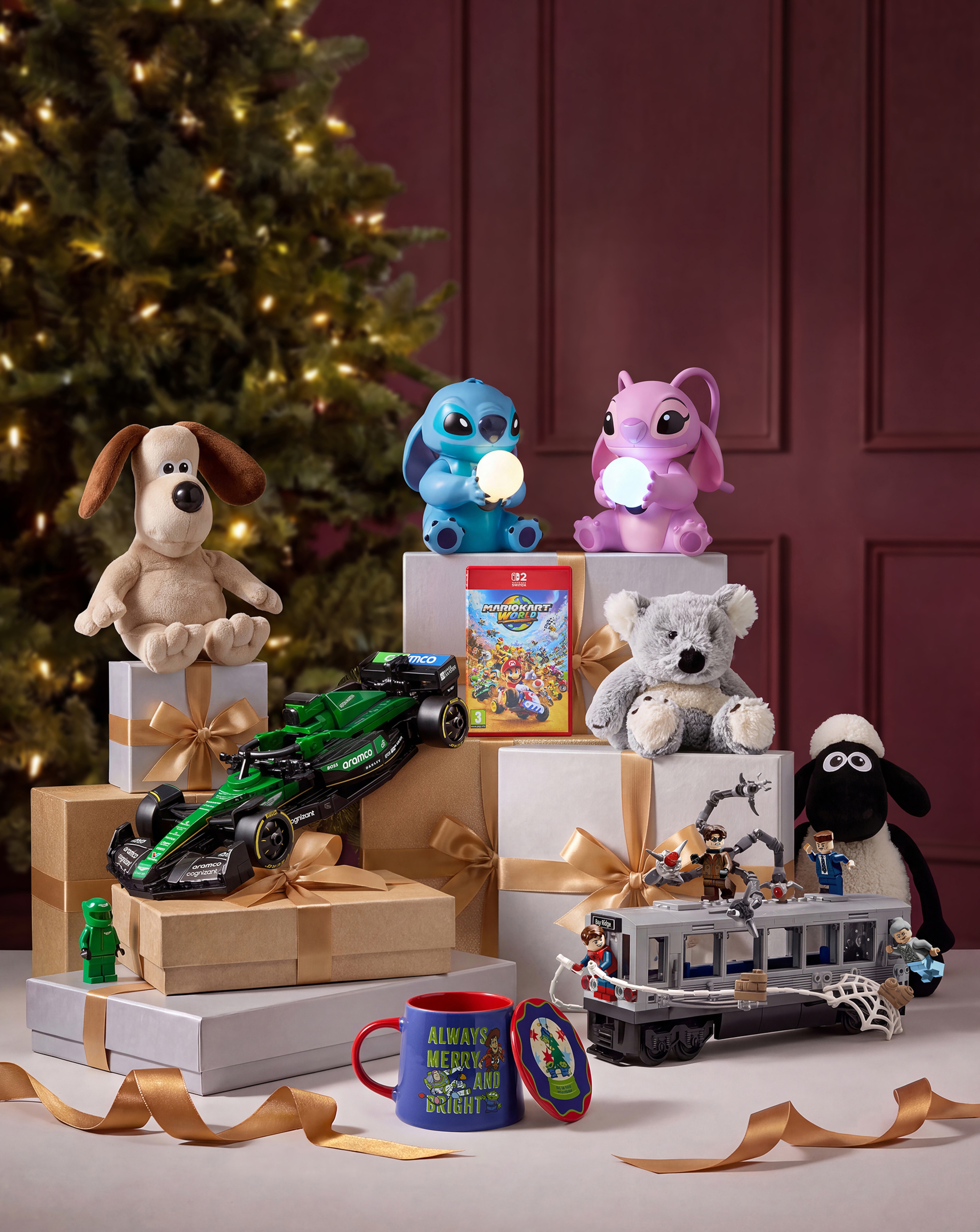 A selection of toys on gift boxes in a room with a burgundy wall and a Christmas tree 
