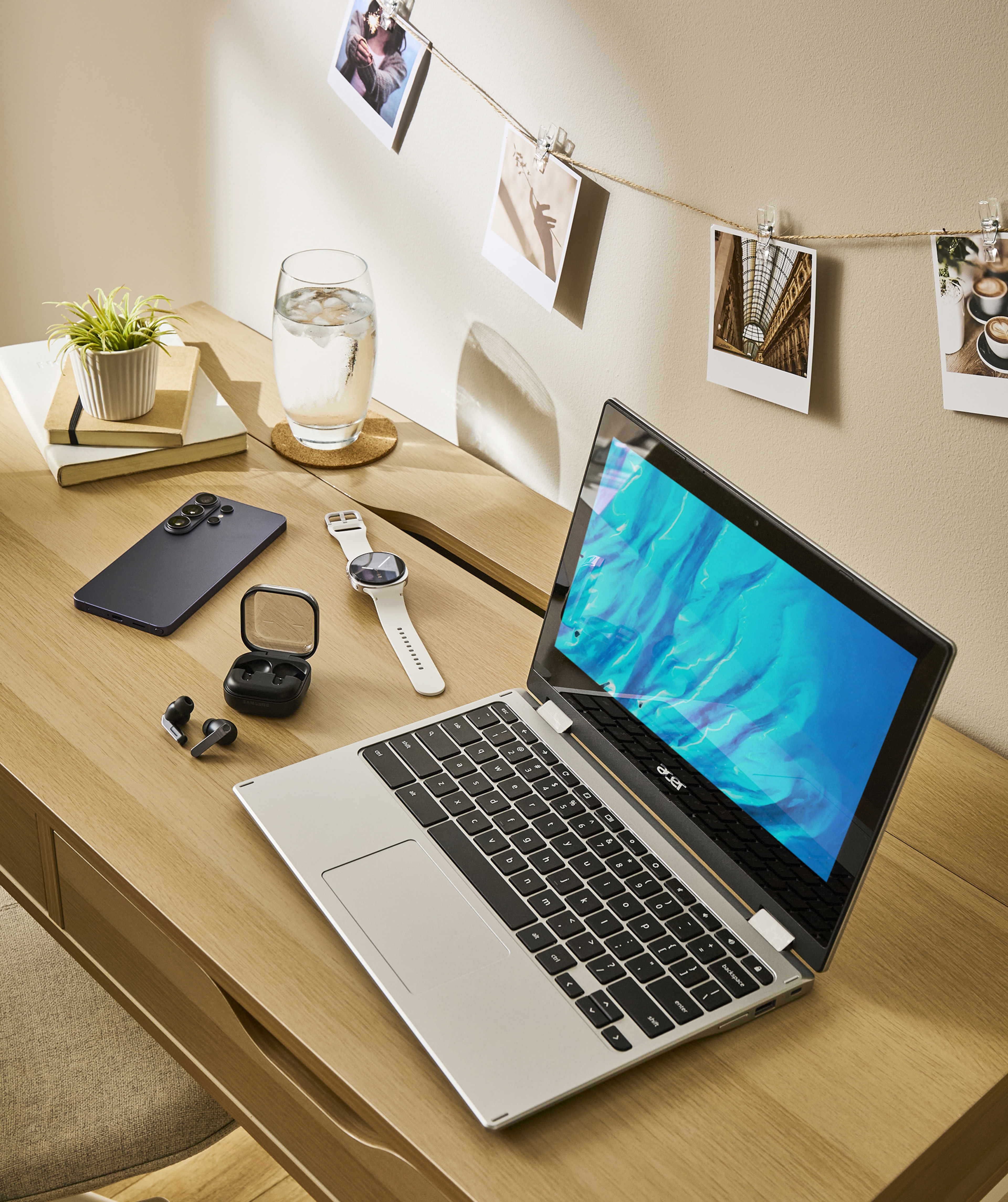 A desk featuring a laptop, a mobile phone, a smart watch and ear buds.