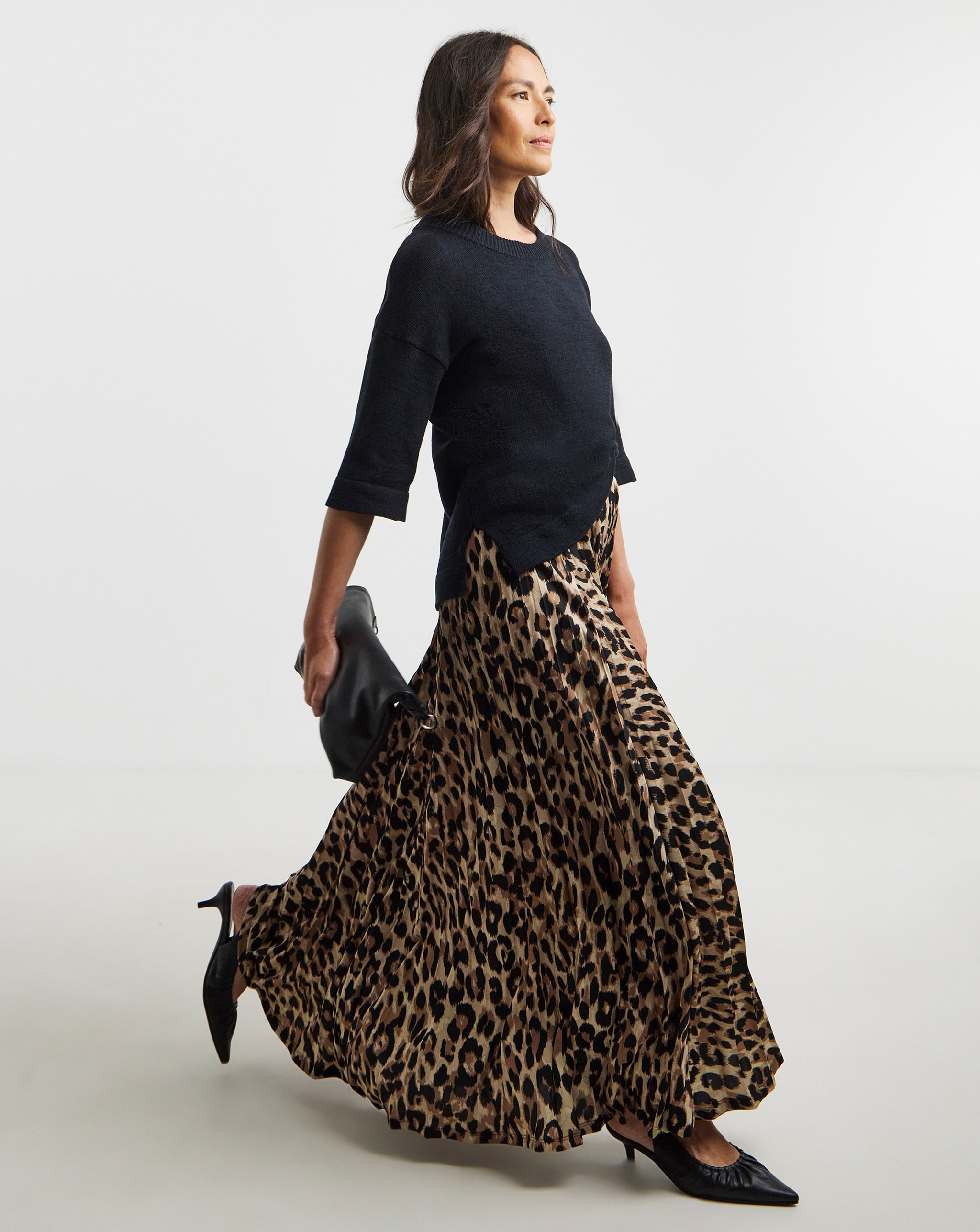Person wearing a black knit top with a flowing leopard-print maxi skirt and black heels, walking forward.