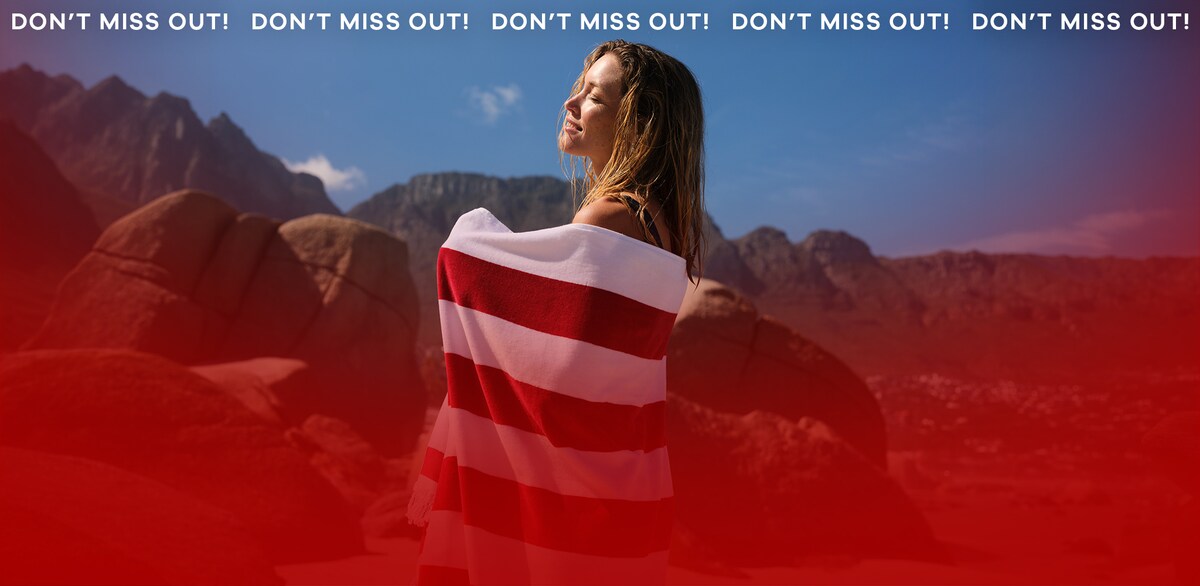 A woman stood looking up to the sun wrapped in a red and white stripey towel.