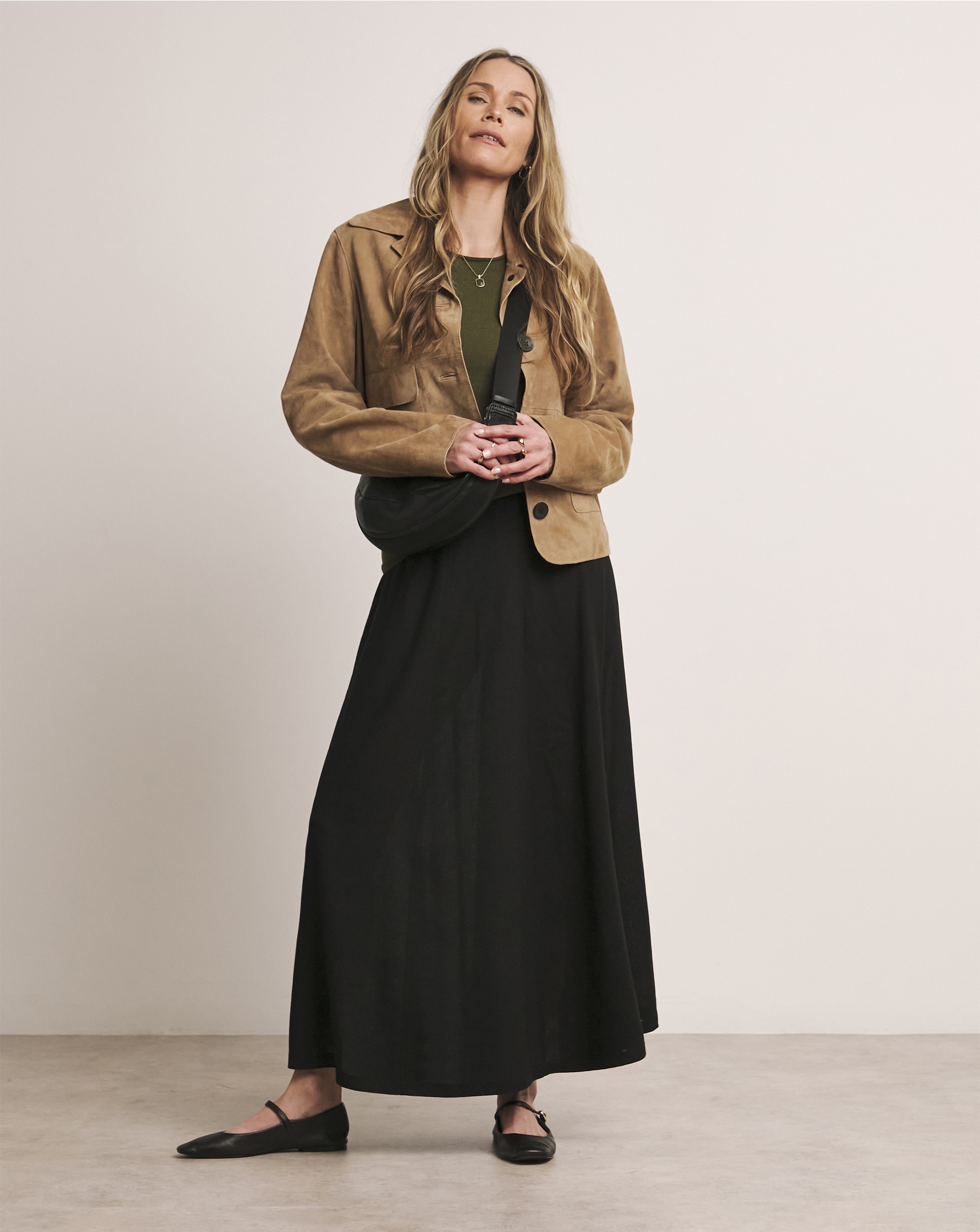 A lady wearing a light brown jacket with a black maxi skirt.