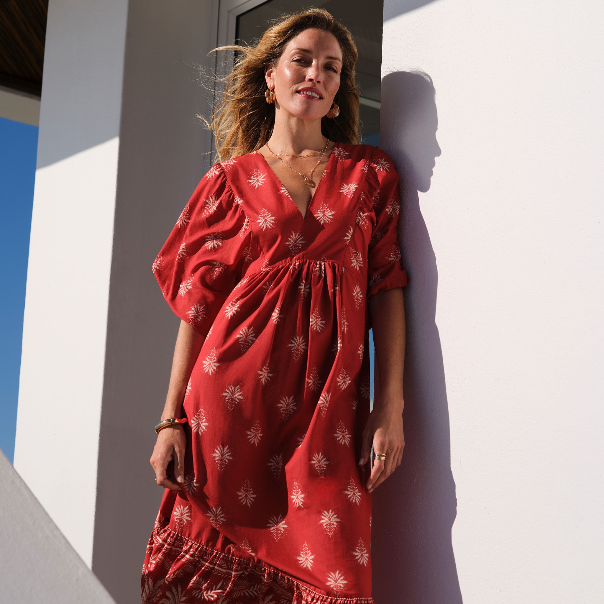 A lady wearing a red dress stood next to a wall.