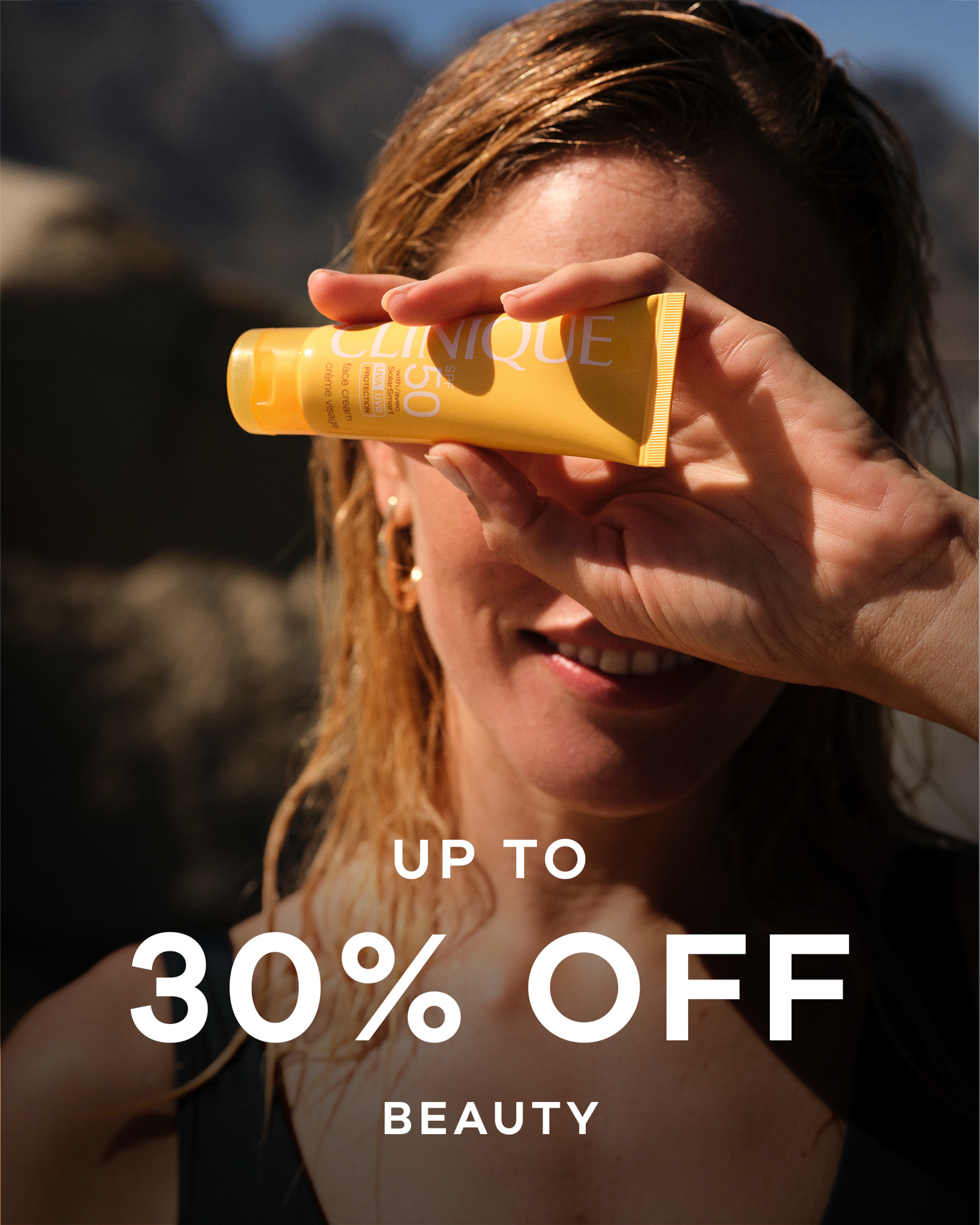 A woman holding up a beauty product in front of her eyes. Up to 30% off beauty