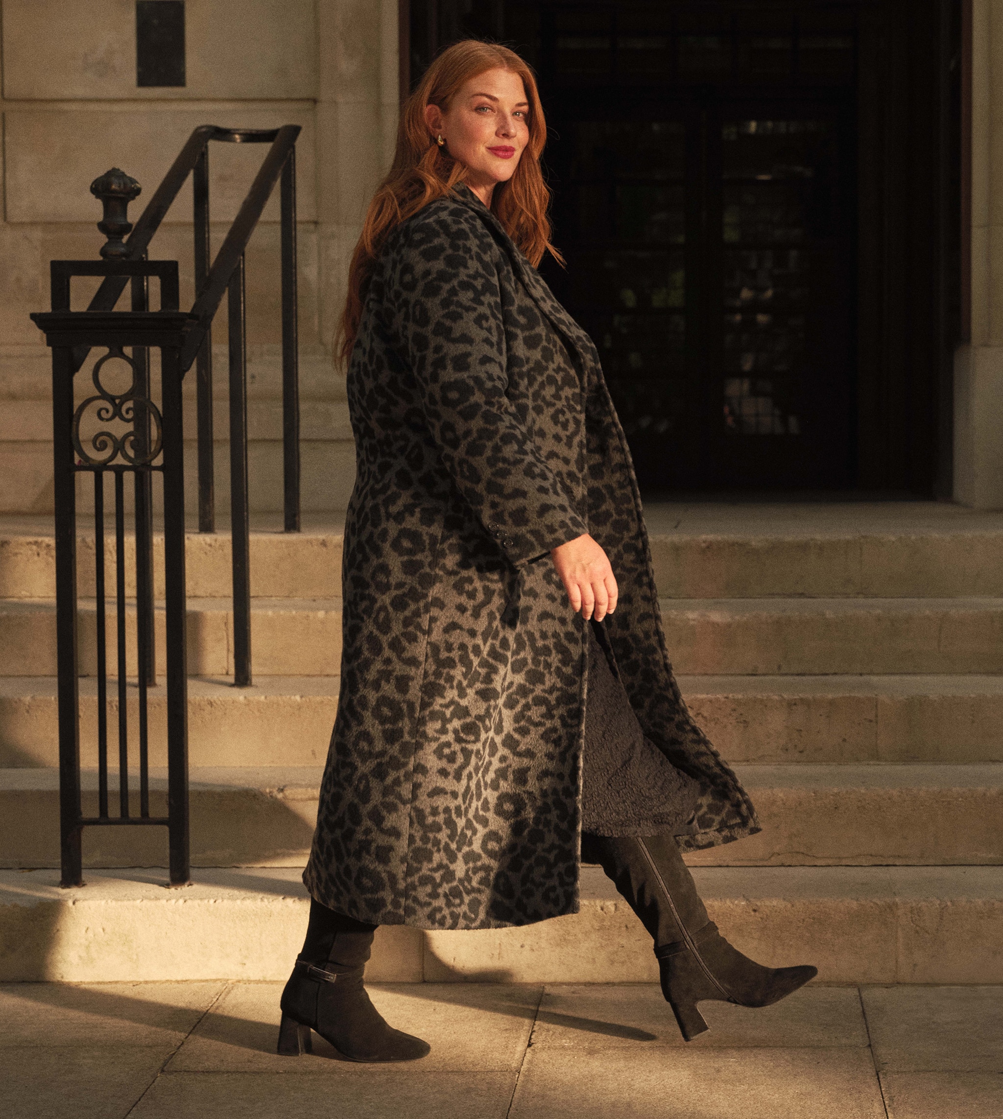 A lady walking outside from left to right wearing a grey and black animal print longline jacket.