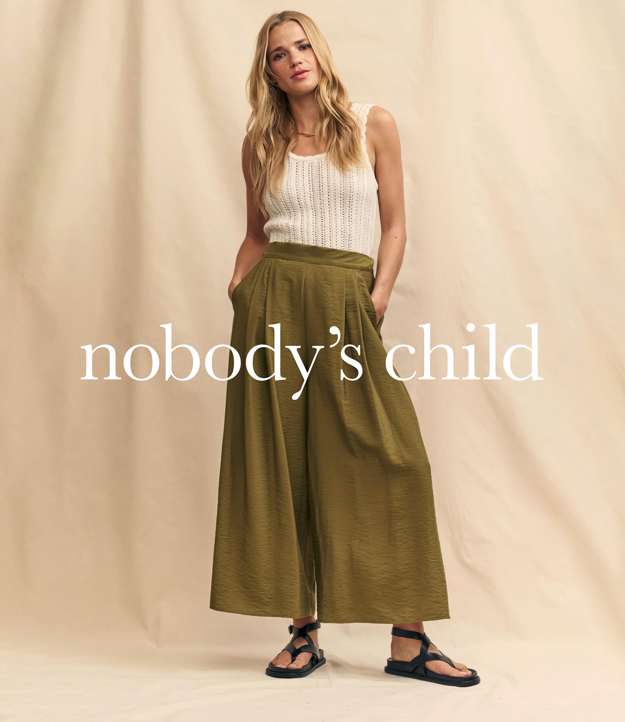 Woman stood in very flared green trousers and white lacy top. Shop Nobody's Child