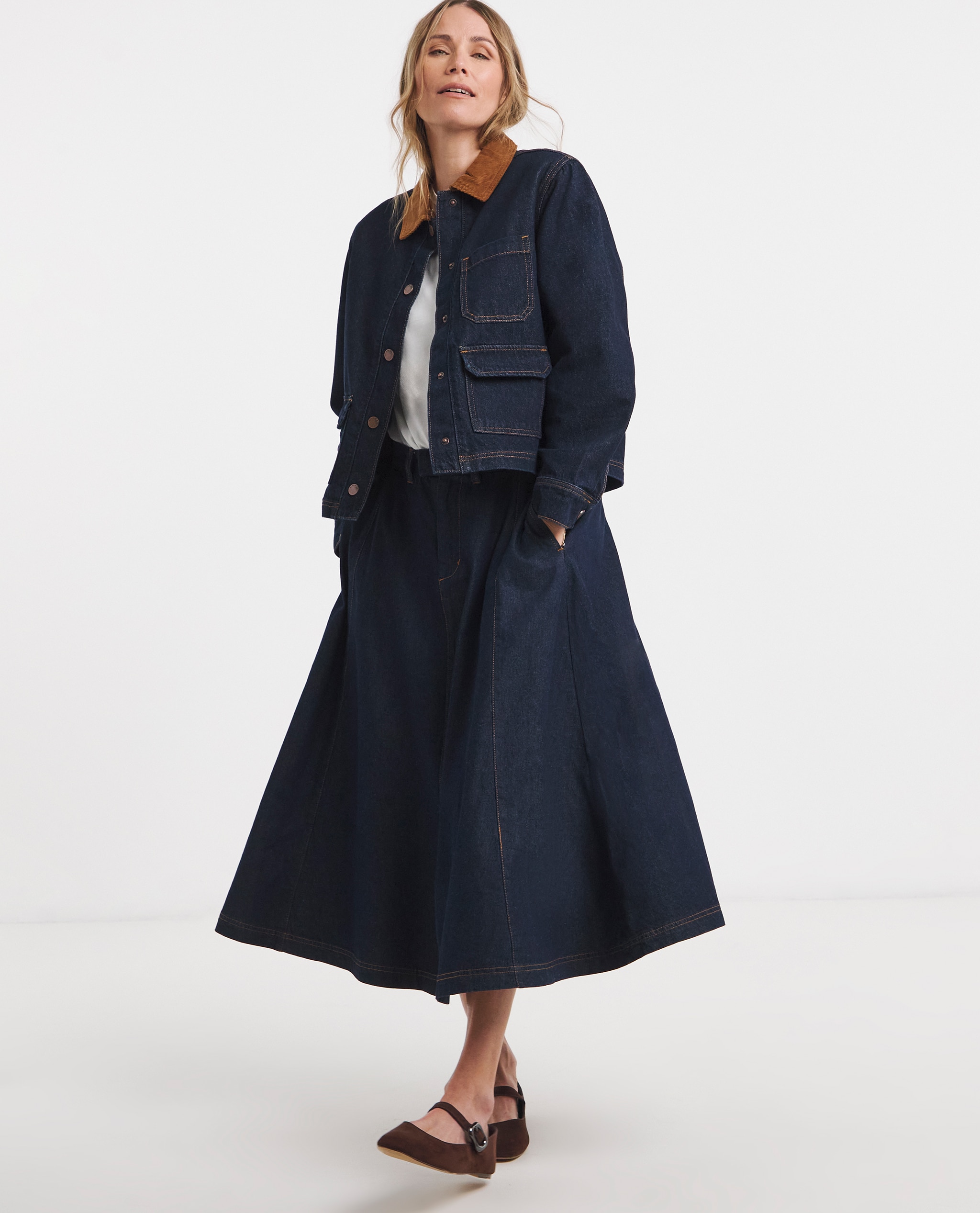 Model is wearing a indigo cord collar barn jacket with a white t-shirt and a indigo seamed full circle midi skirt with ballet flats.