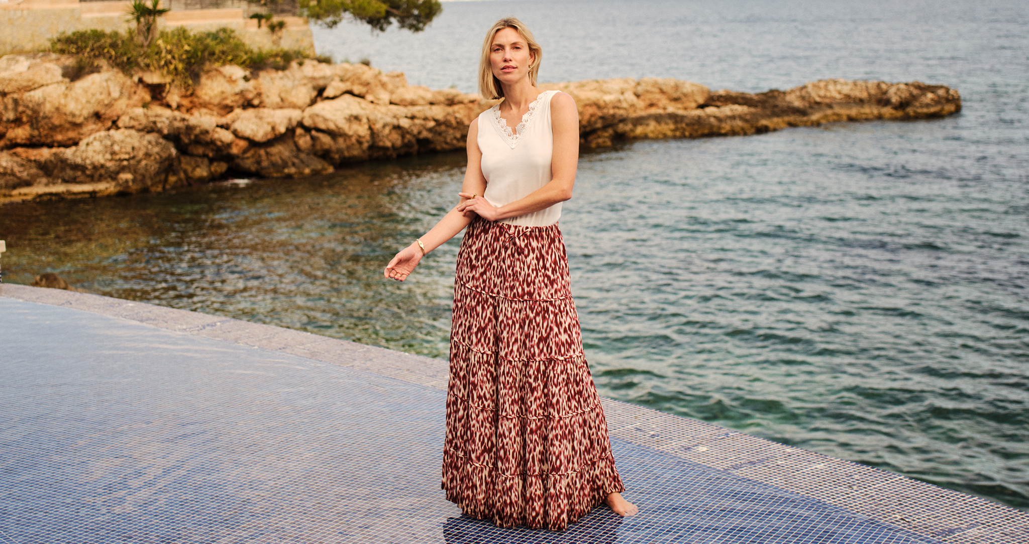 A lady wearing a white vest top with a red skirt stood by the sea.