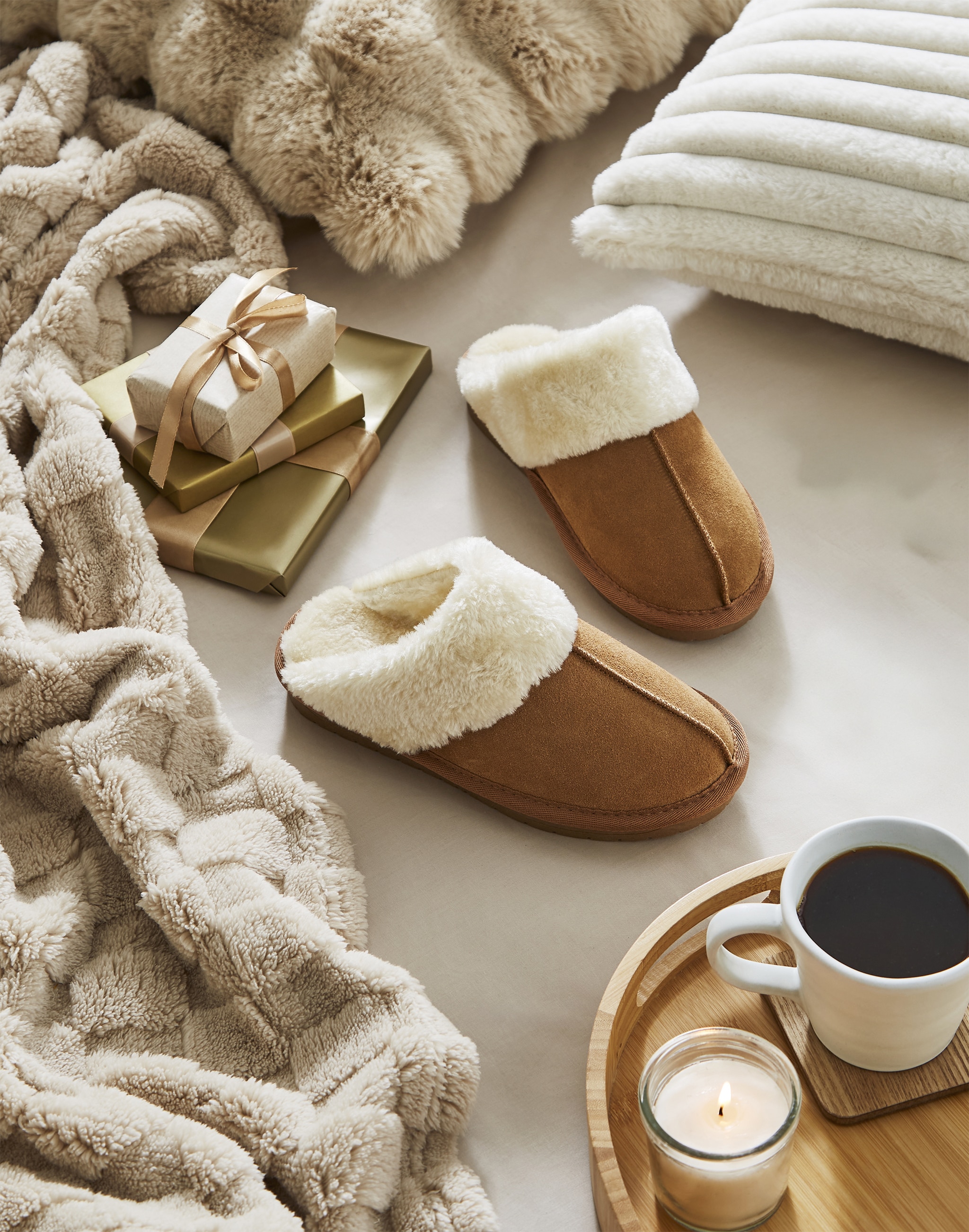 A pair of brown suede mule slippers next to some gifts and a tray with coffee