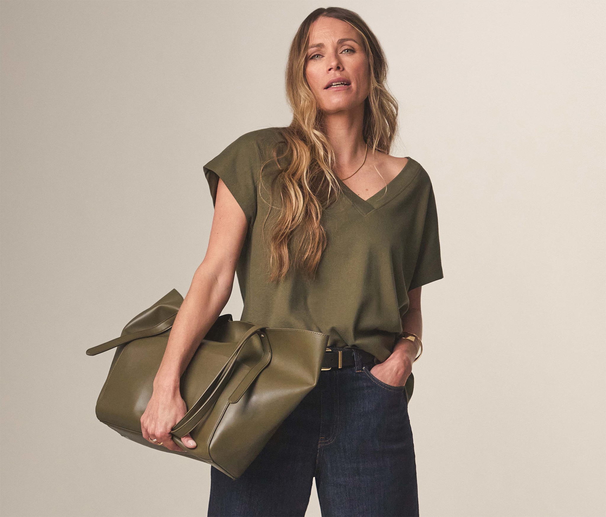 A lady wearing a green top with blue trousers holding a green bag.