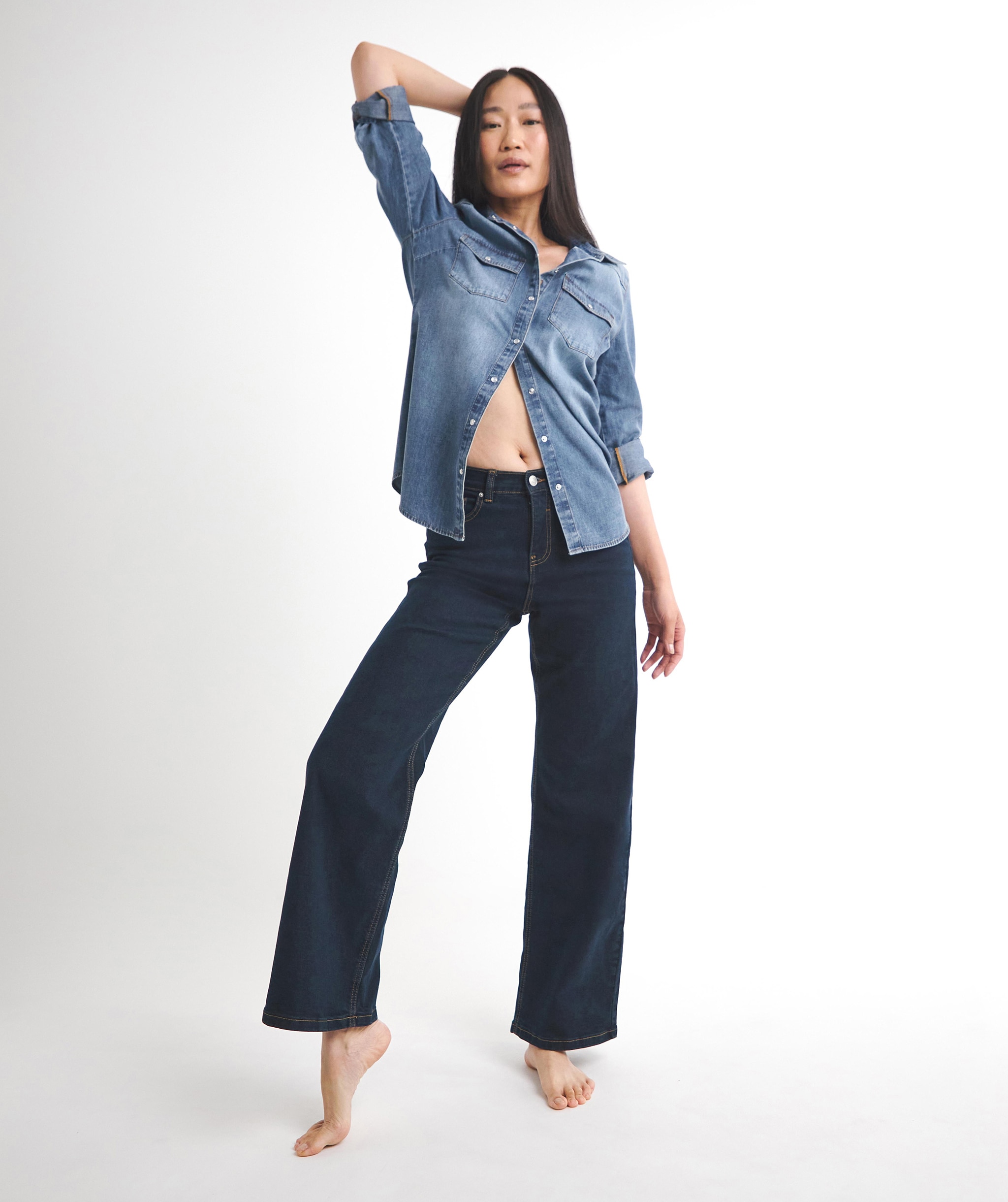 WOMAN STOOD WEARING A BLUE DENIM SHIRT AND LOOSE FIT BLACK TROUSERS