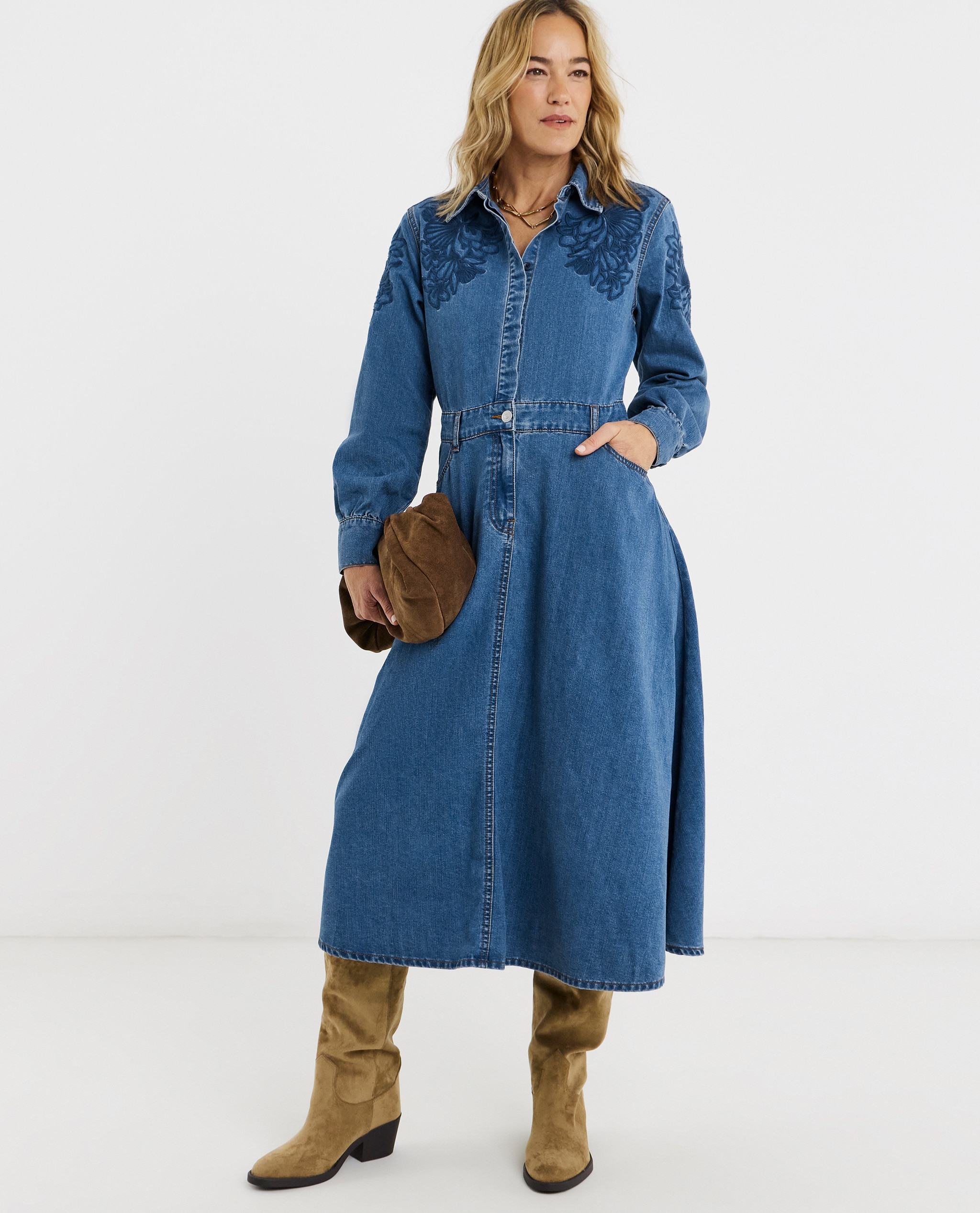 Model is wearing a blue embroidered denim midi dress with a pair of slouch boots and handbag.