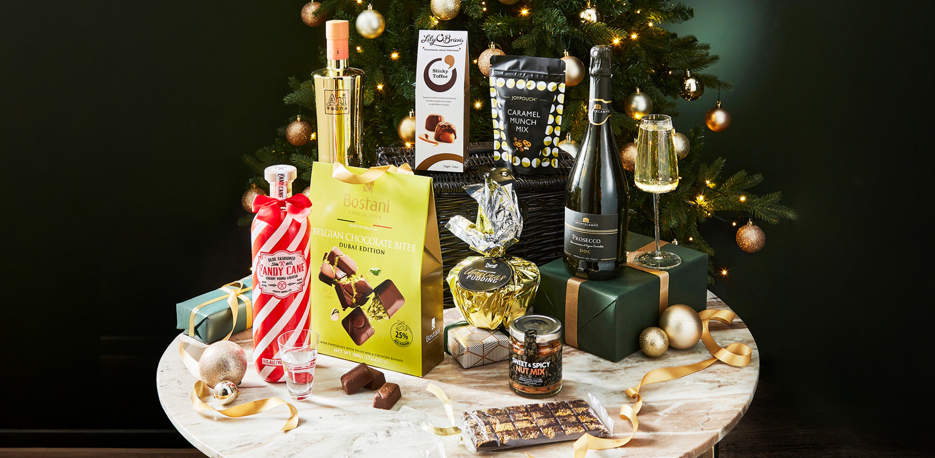 A range of Christmas gifts on a table with a Christmas tree behind.