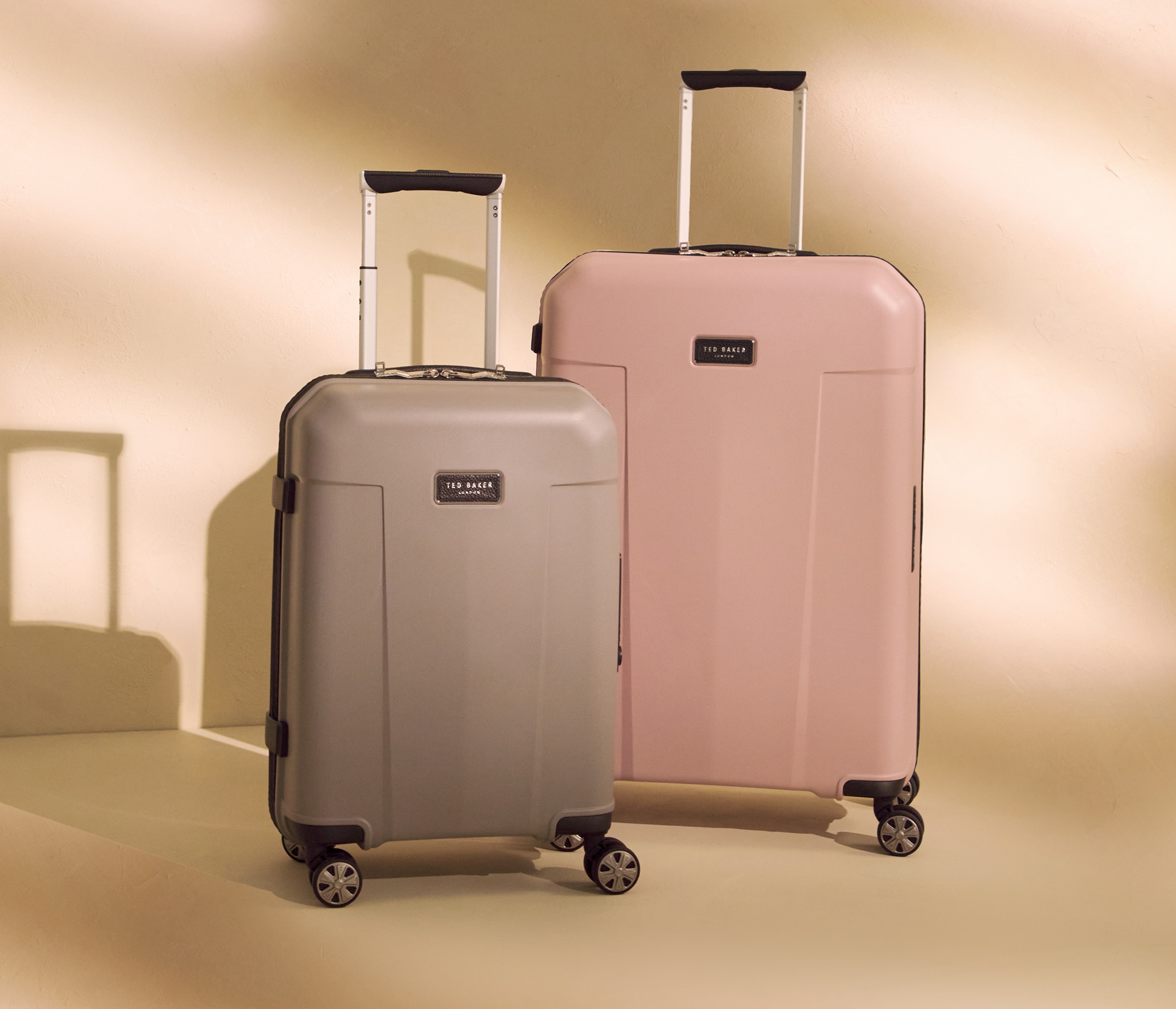 A coffee coloured suitcase next to a larger pink suitcase in a sandy /. gold room.