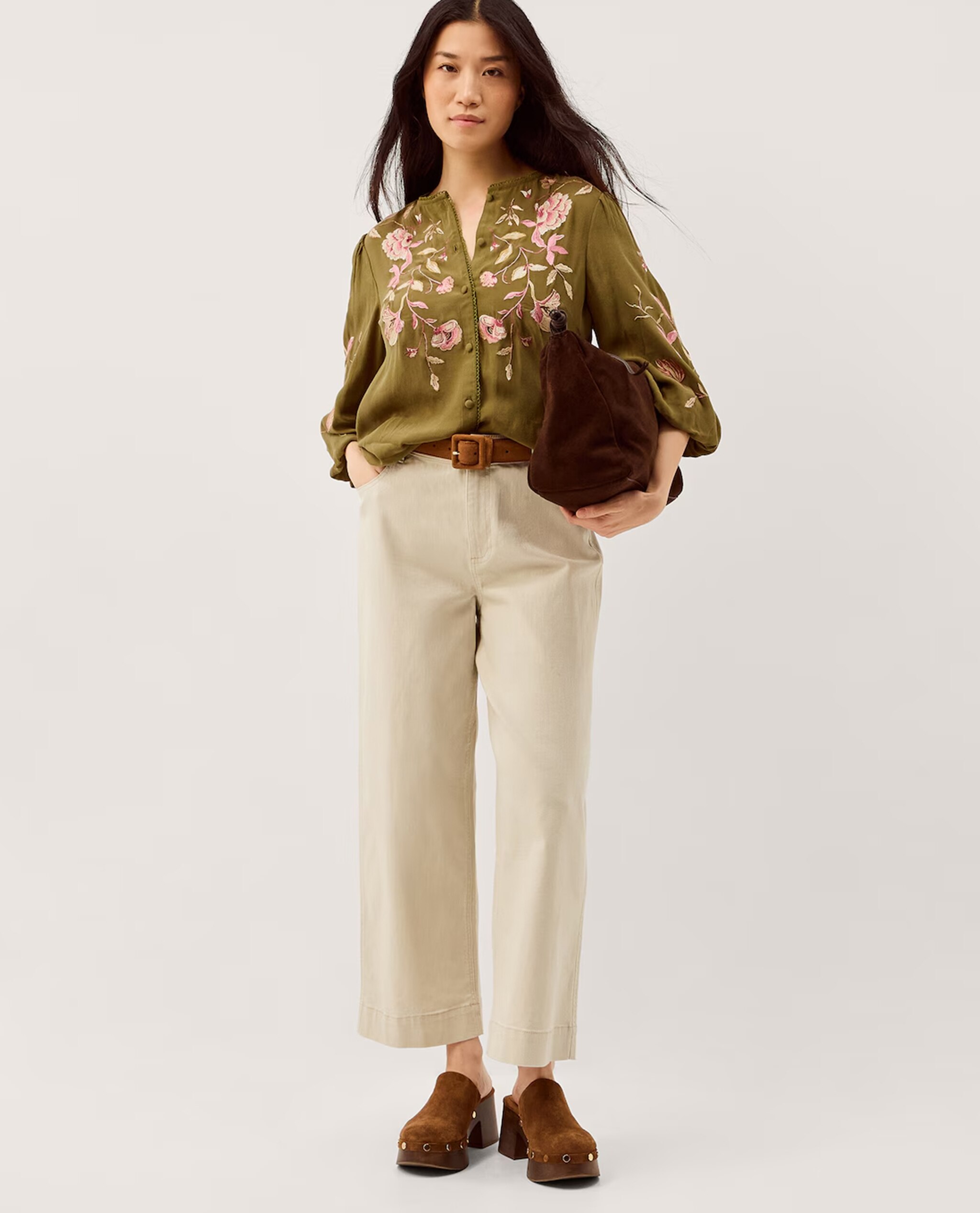 Model is wearing a Monsoon Amelie floral embroidered blouse with cream trousers and a tan belt.