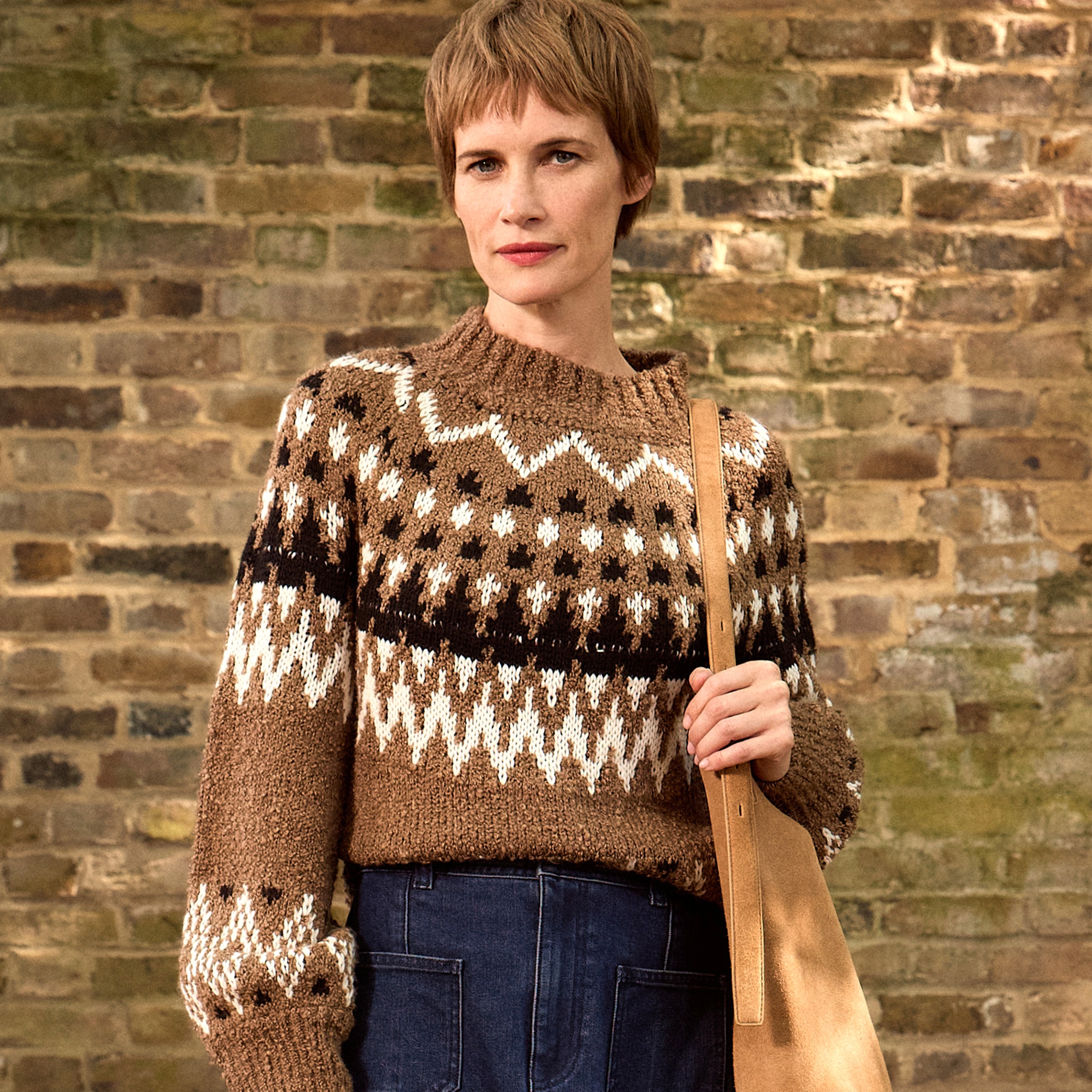 A lady stood wearing a brown crew neck jumper with black and white zig zag patterns across it.