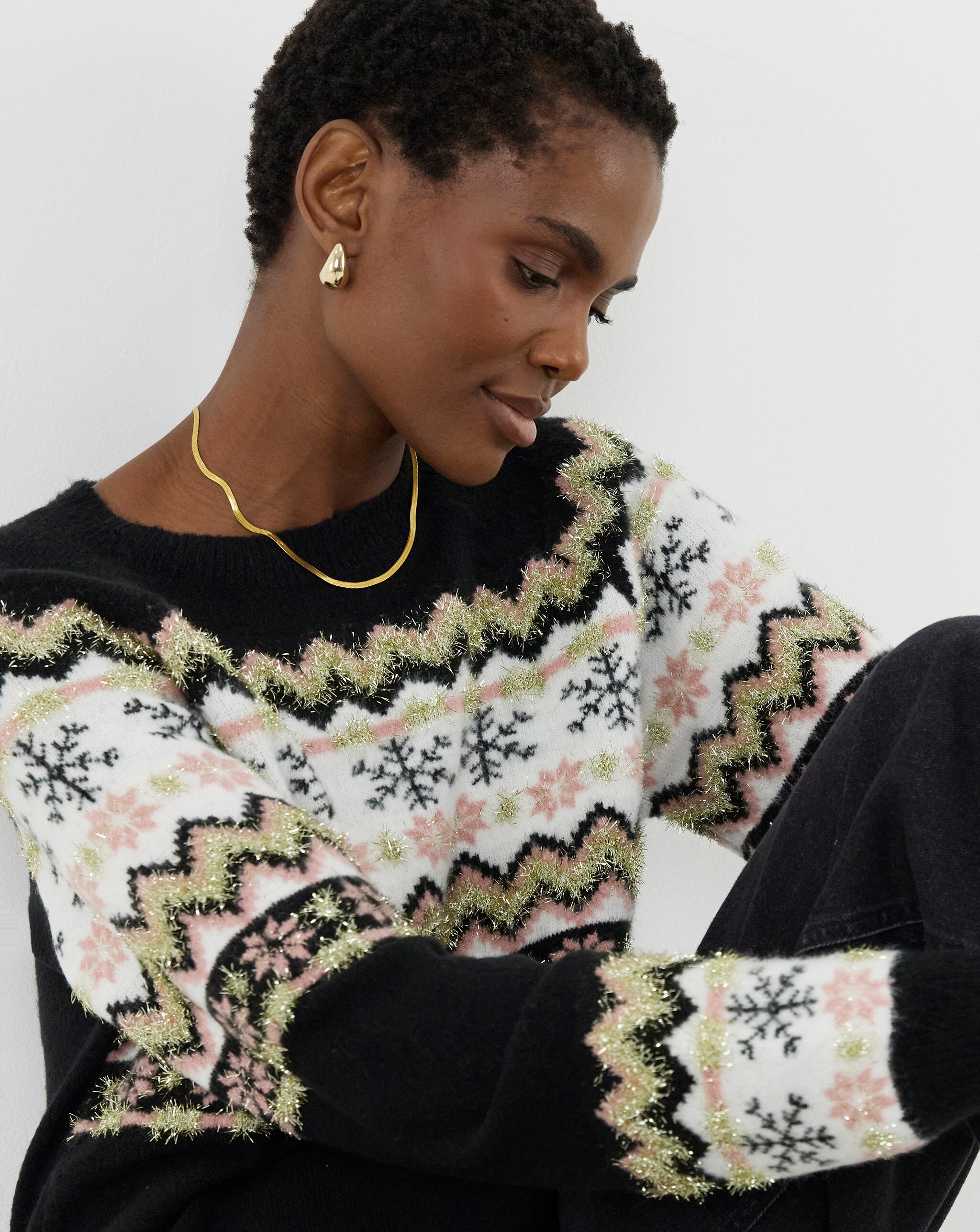 Lady sat down wearing a fair black, gold, white and pink isle jumper.