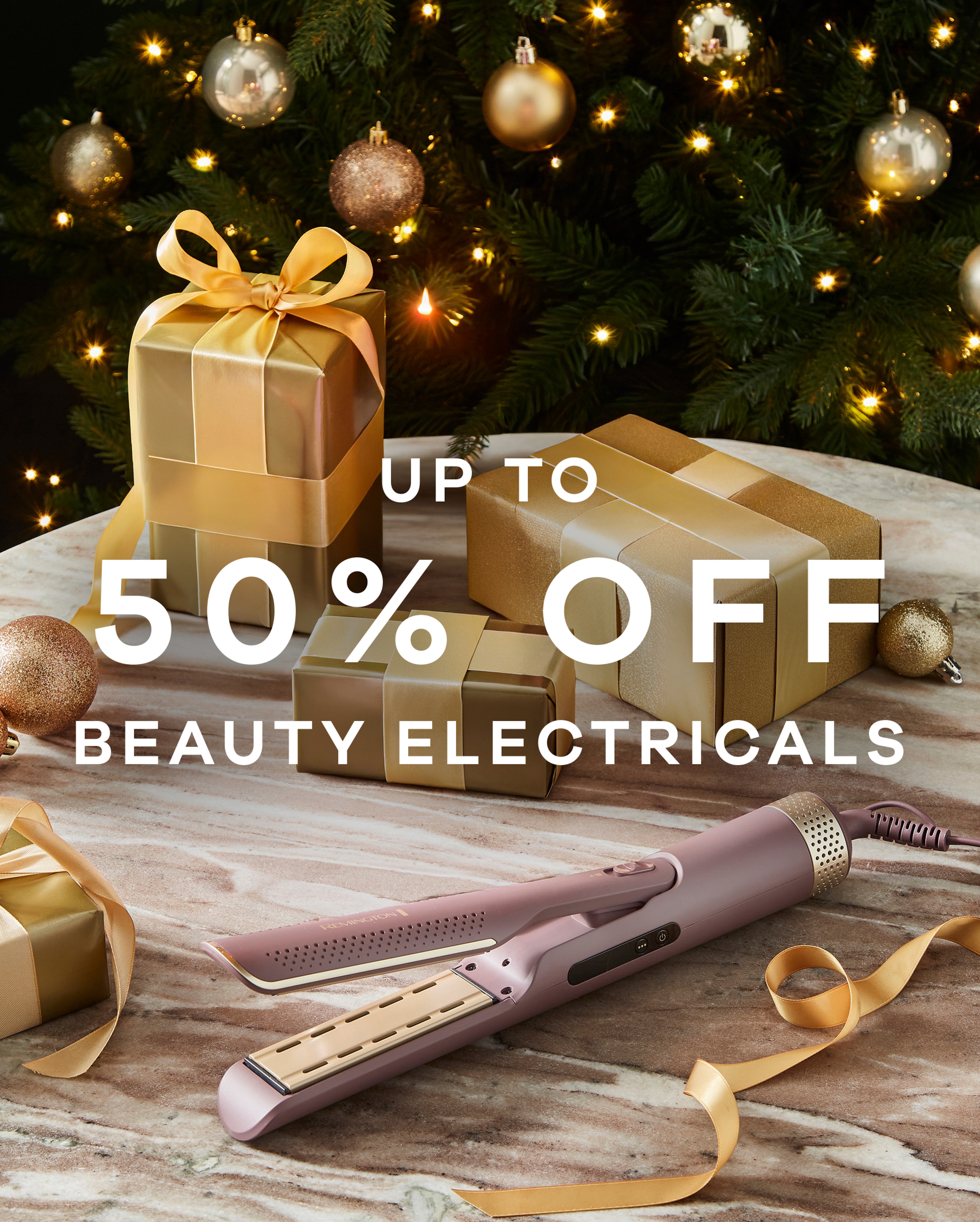 Up to 50% off beauty electricals text overlaid on an image with hair straighteners on a table with a Christmas tree in the background.
