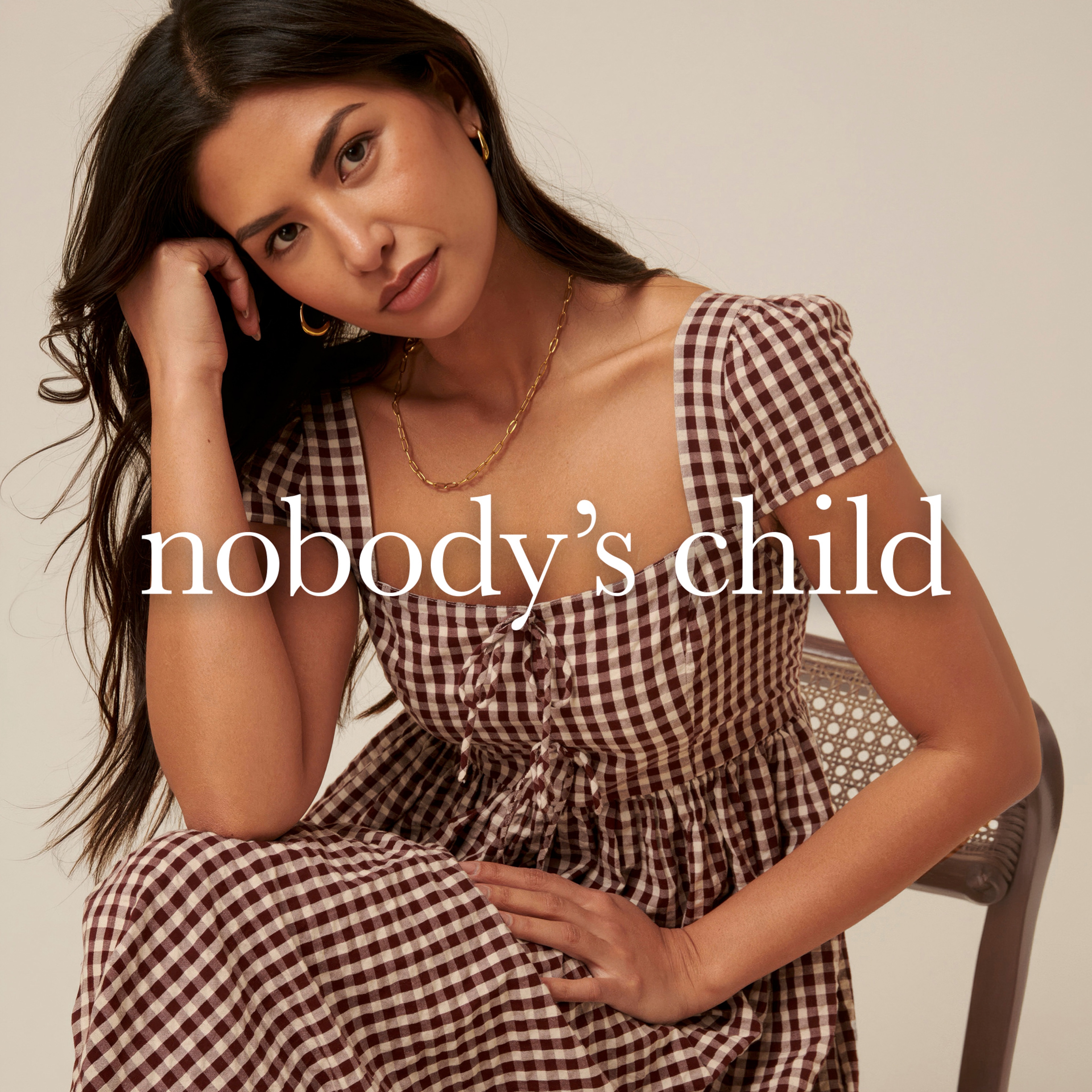 A lady sat resting her head on her hand wearing a Nobody's Child dress.